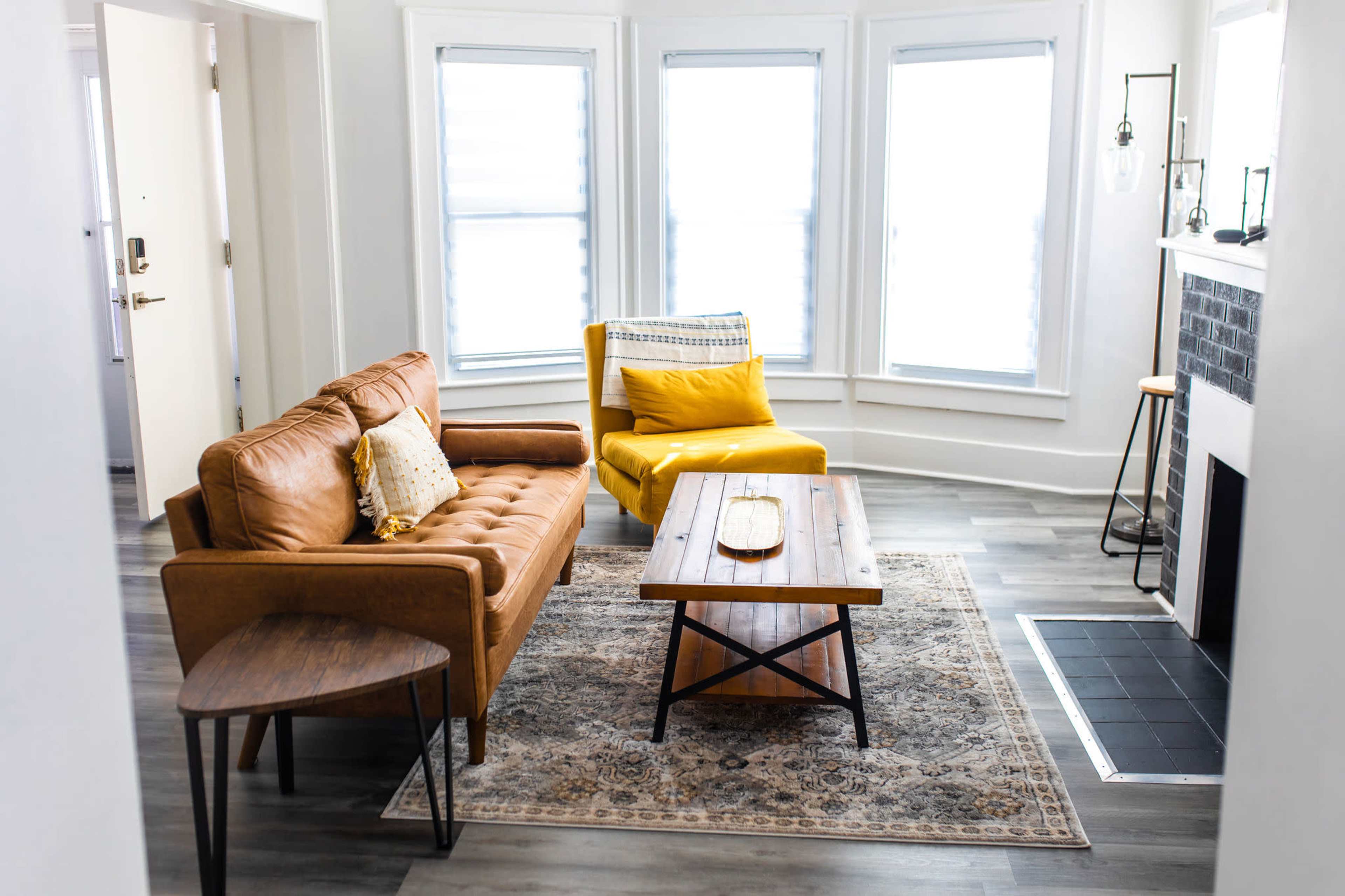 A cozy living room features a brown leather sofa, a wooden coffee table, a yellow armchair, and a patterned rug.
