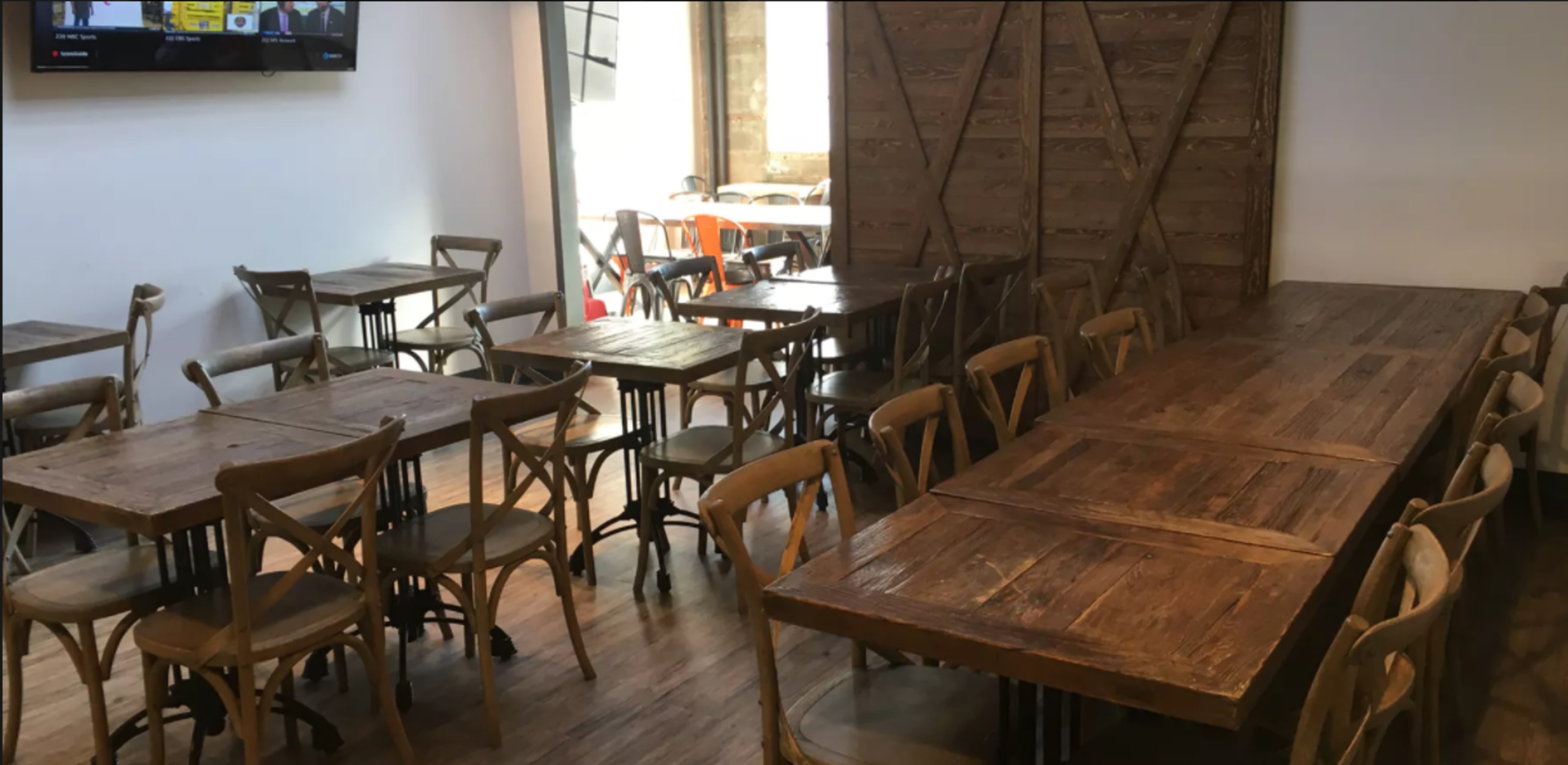 A spacious café interior featuring several wooden tables and chairs arranged throughout the room, with a large communal table at the center.