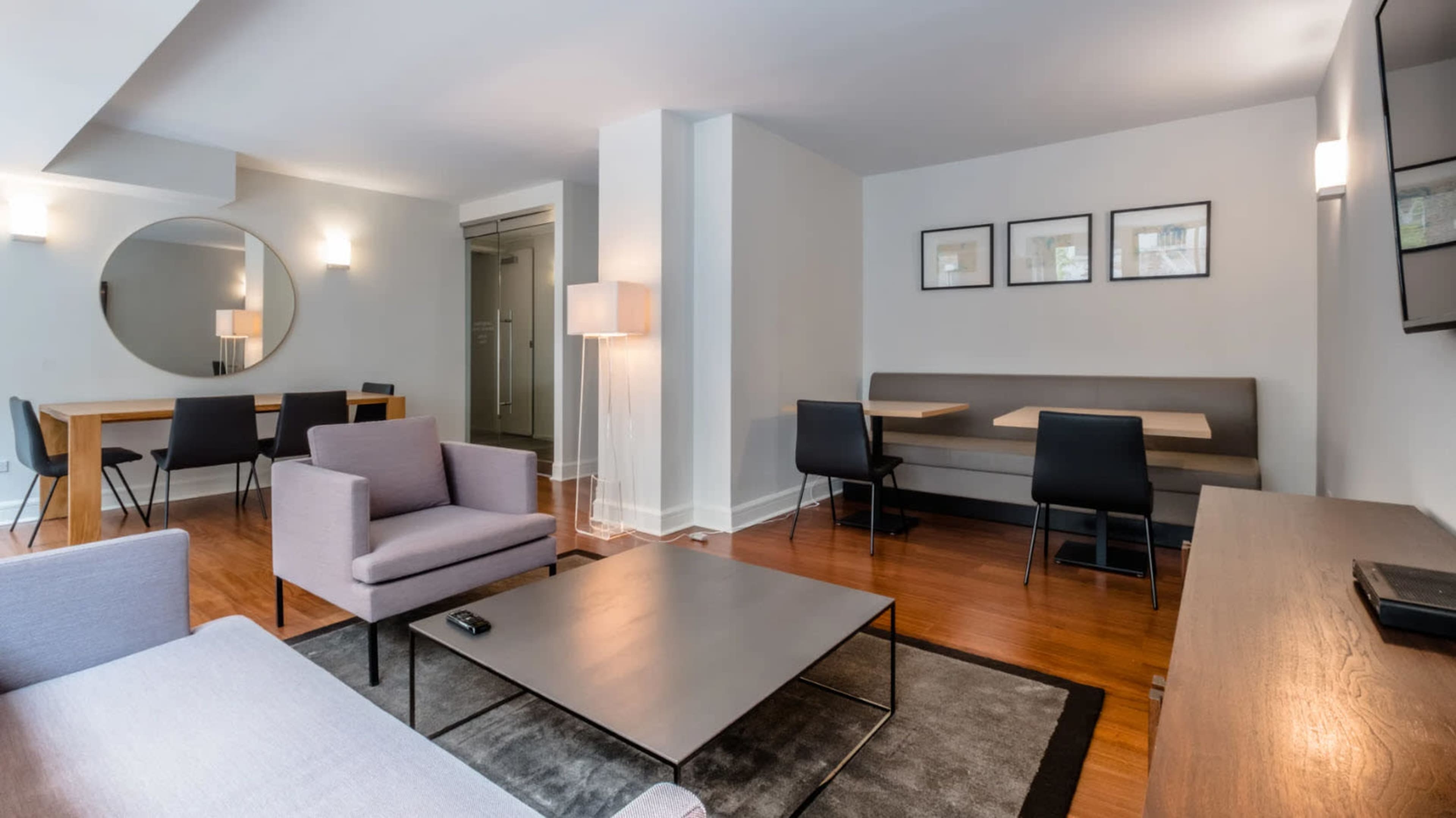 A modern living area with a seating arrangement, a dining table, and a large circular mirror on the wall.