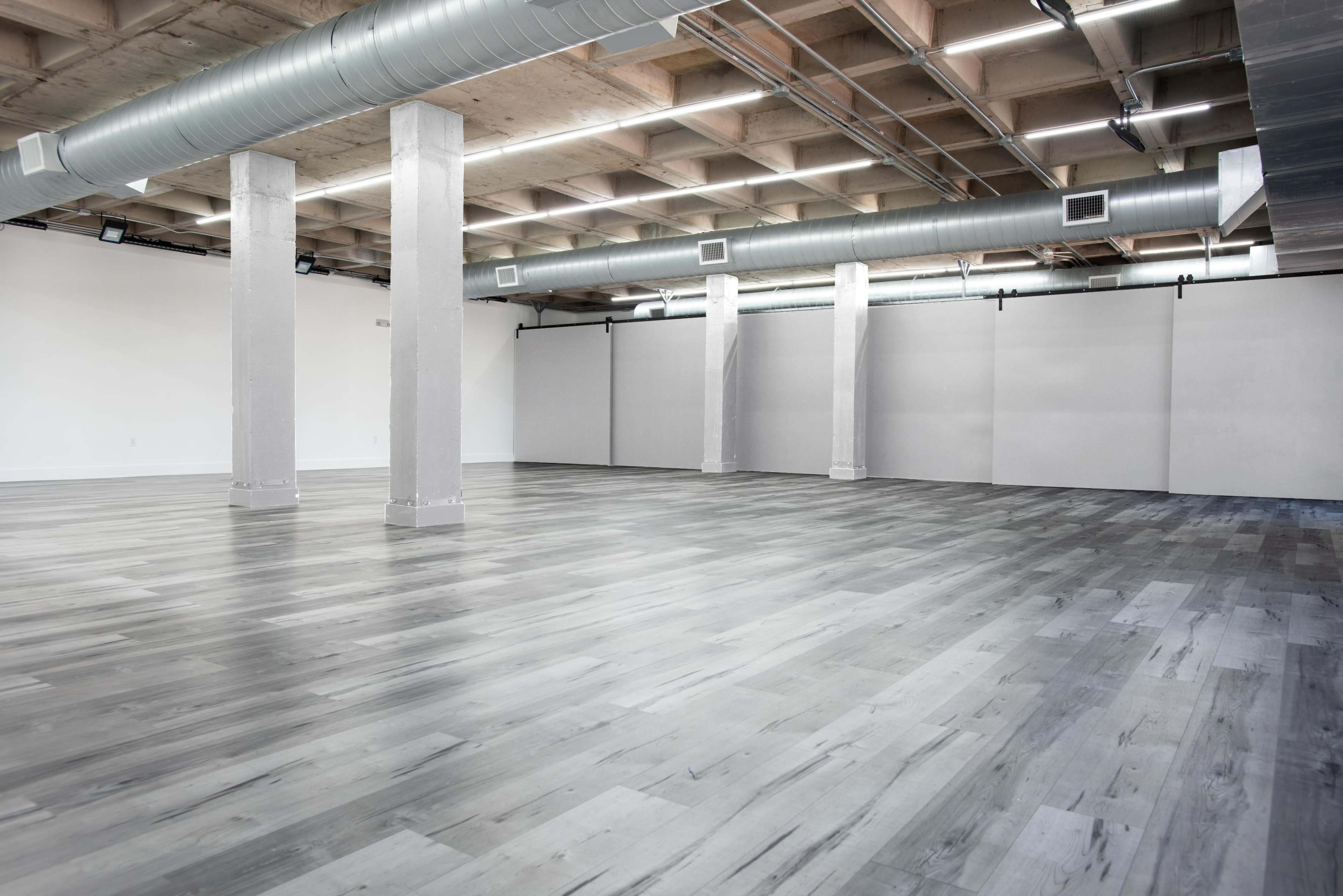The image shows a spacious, empty interior with polished wooden floors and exposed ductwork running along the ceiling.