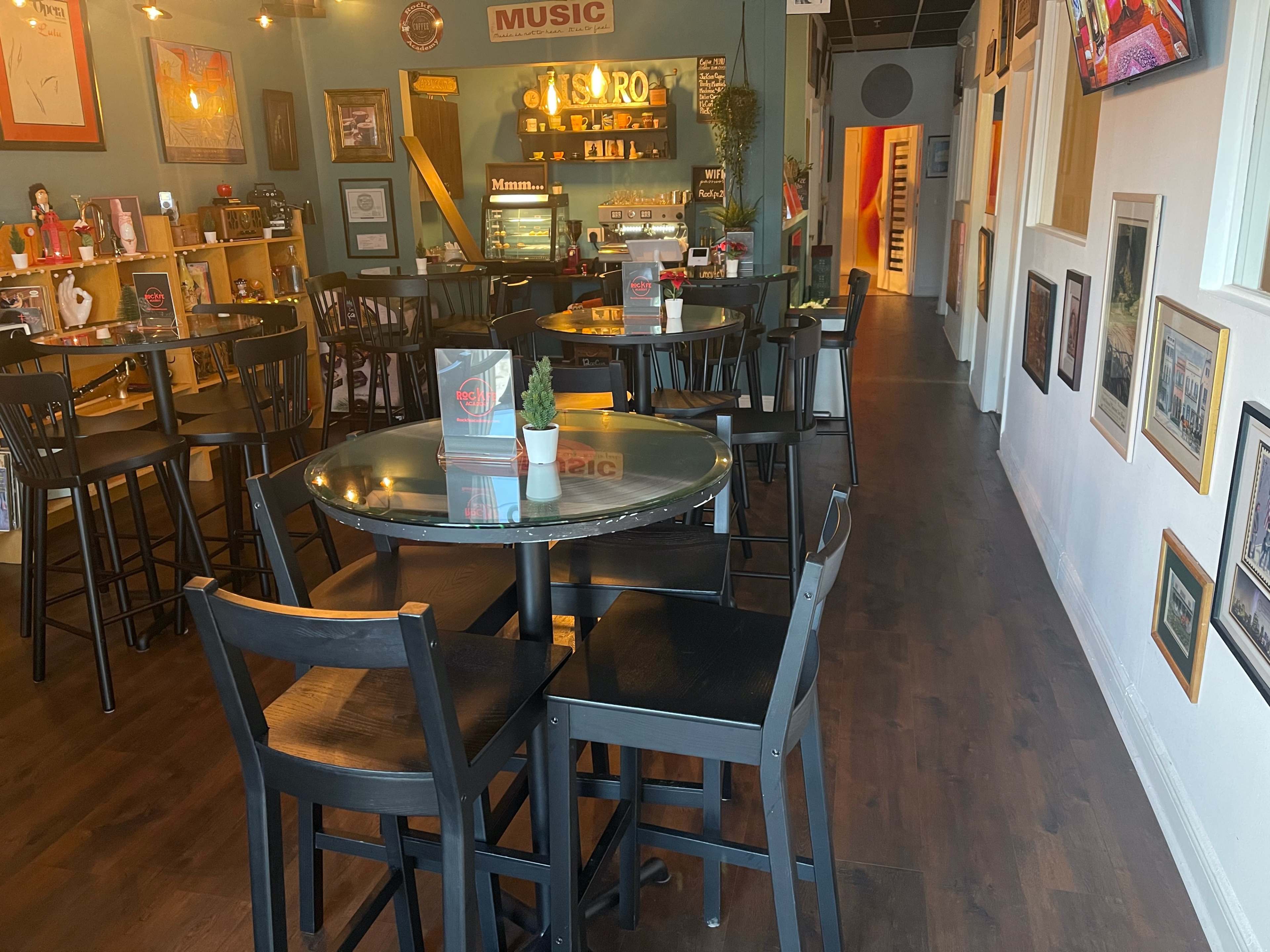 The image shows a restaurant interior featuring several black tables and chairs, decorated walls with framed pictures, and a display area with various items.