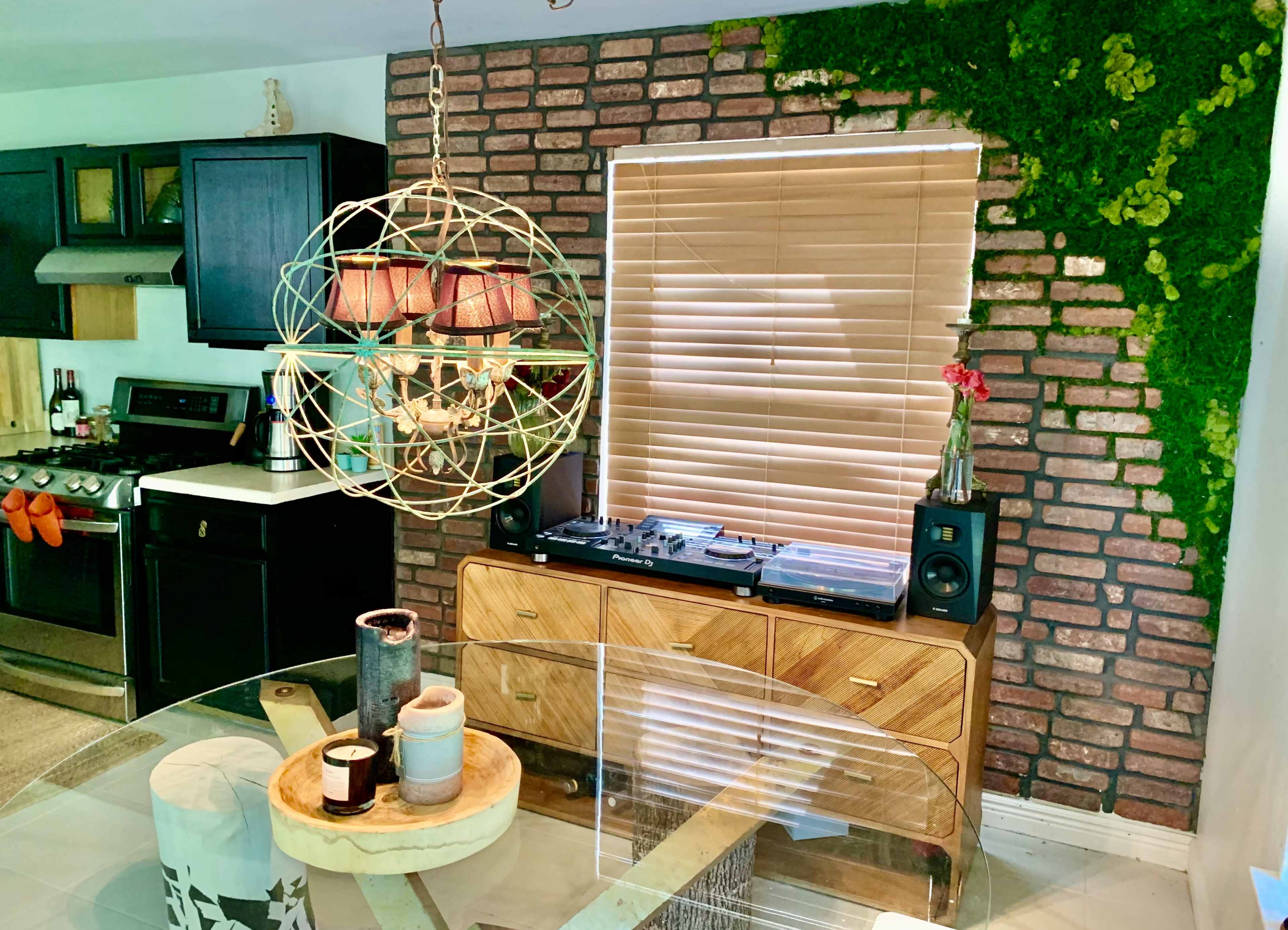 A modern kitchen area with a brick wall, a wooden cabinet holding a record player, and a round dining table with candles.