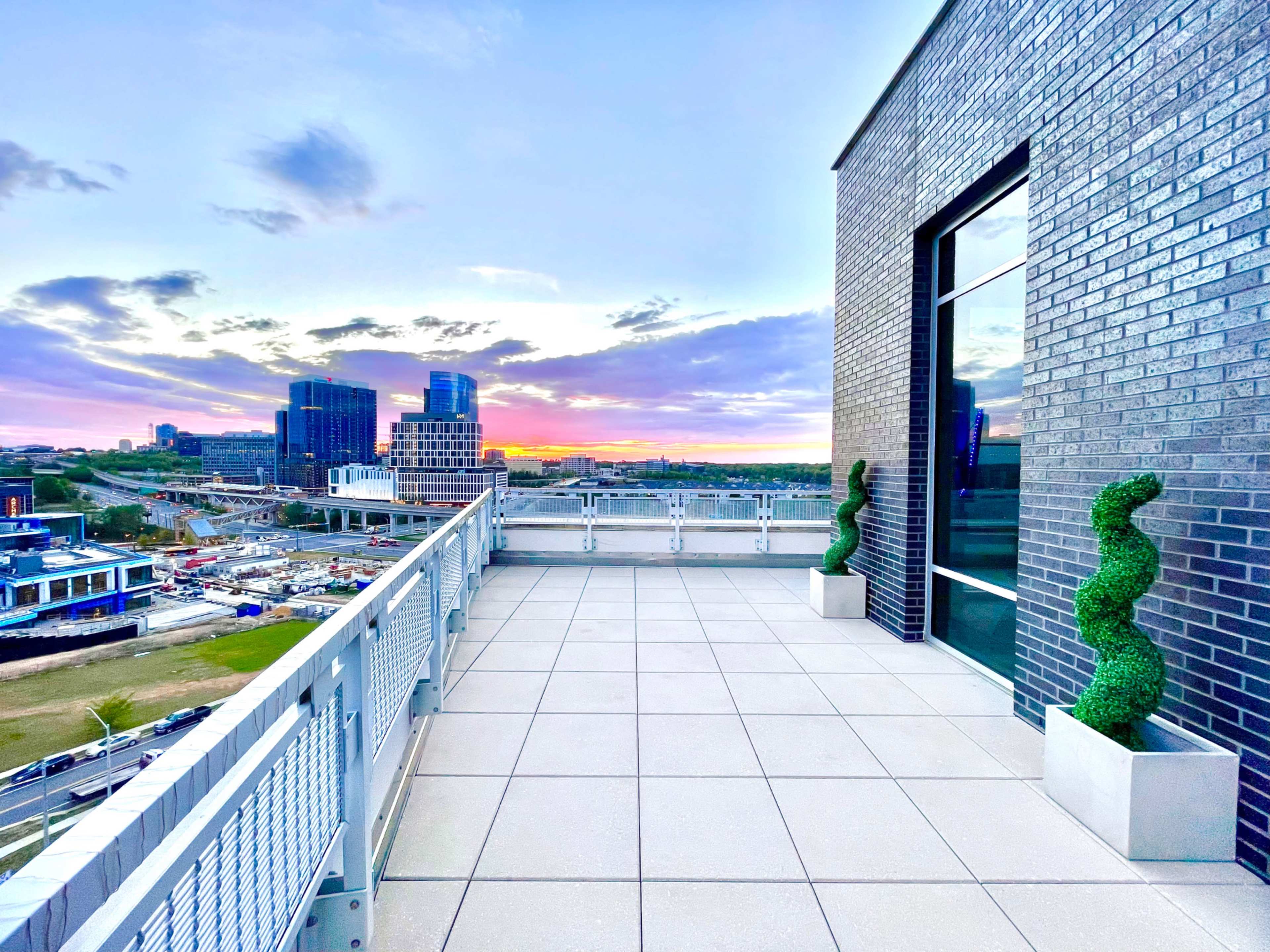 A modern balcony with decorative topiary and a view of a city skyline at sunset.