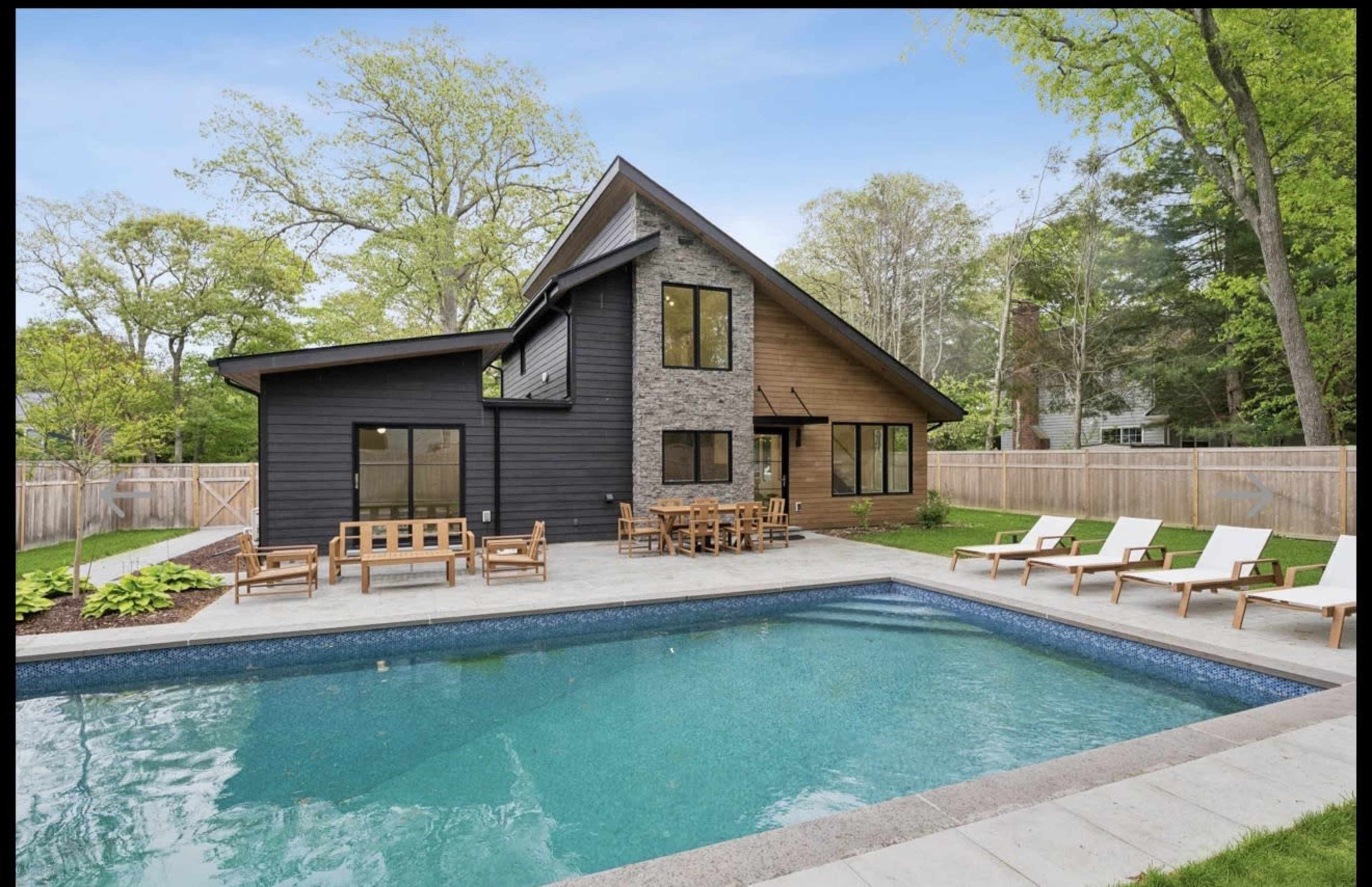 The image features a modern house with a stone and wood facade adjacent to a swimming pool, surrounded by lounge chairs and a landscaped yard.