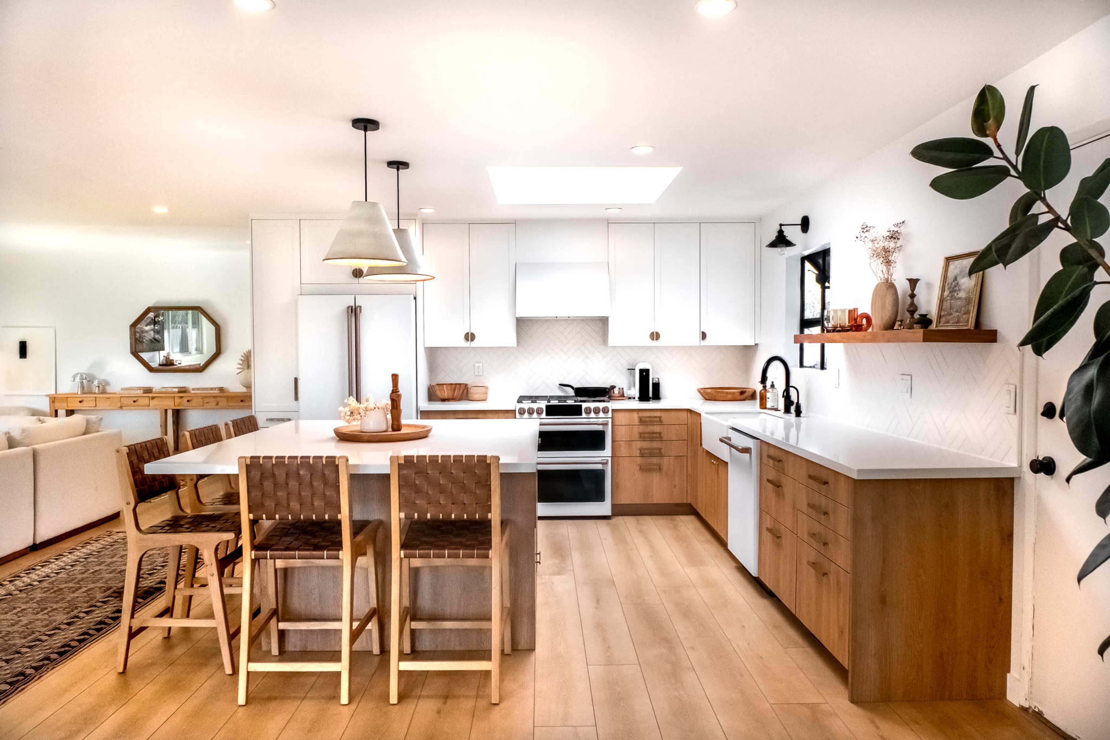 A modern kitchen features white cabinets, a central island with seating, and stainless steel appliances, with a dining area visible in the background.