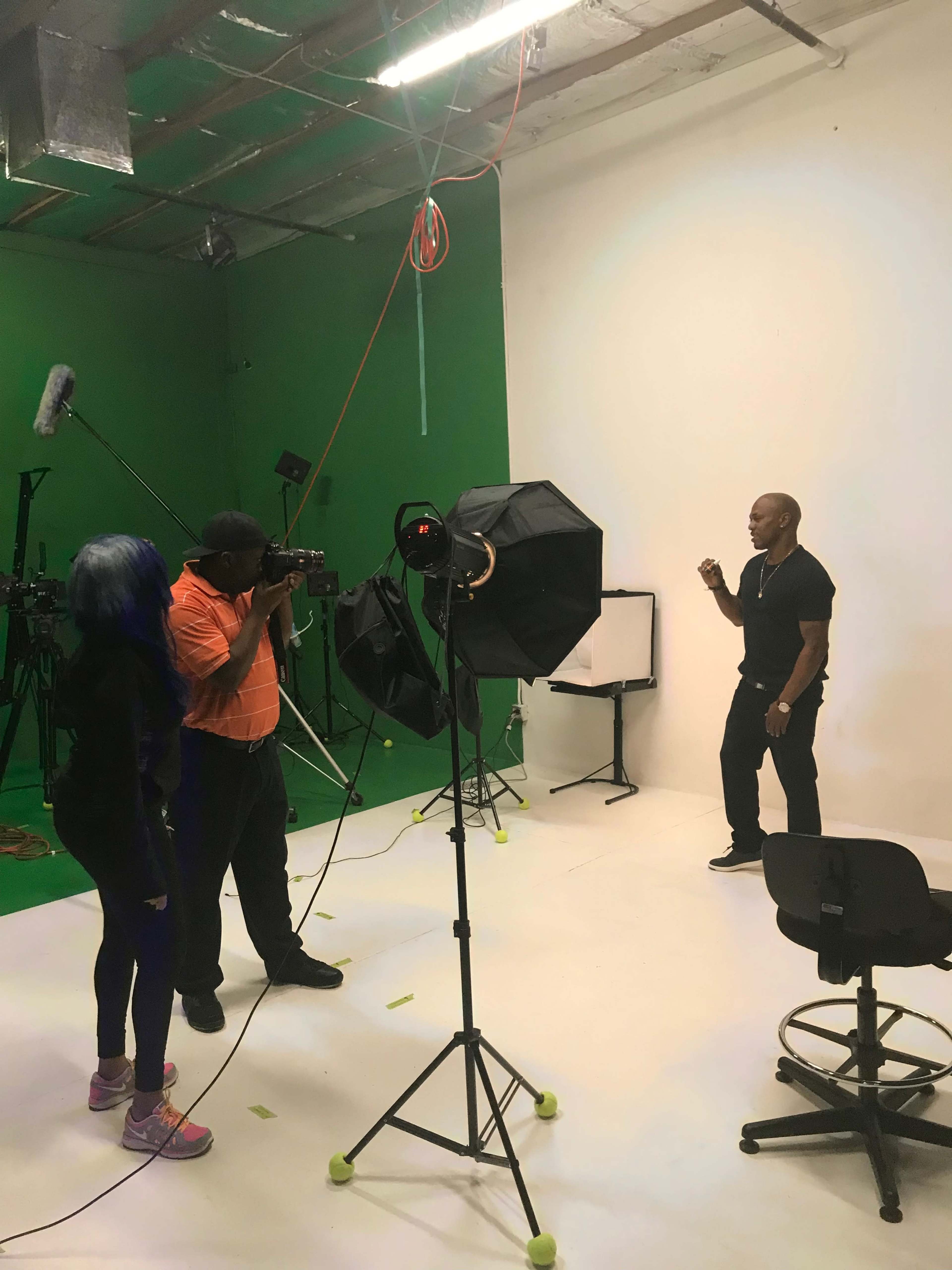 A photographer captures a man posing in a studio with a green screen and various filming equipment.