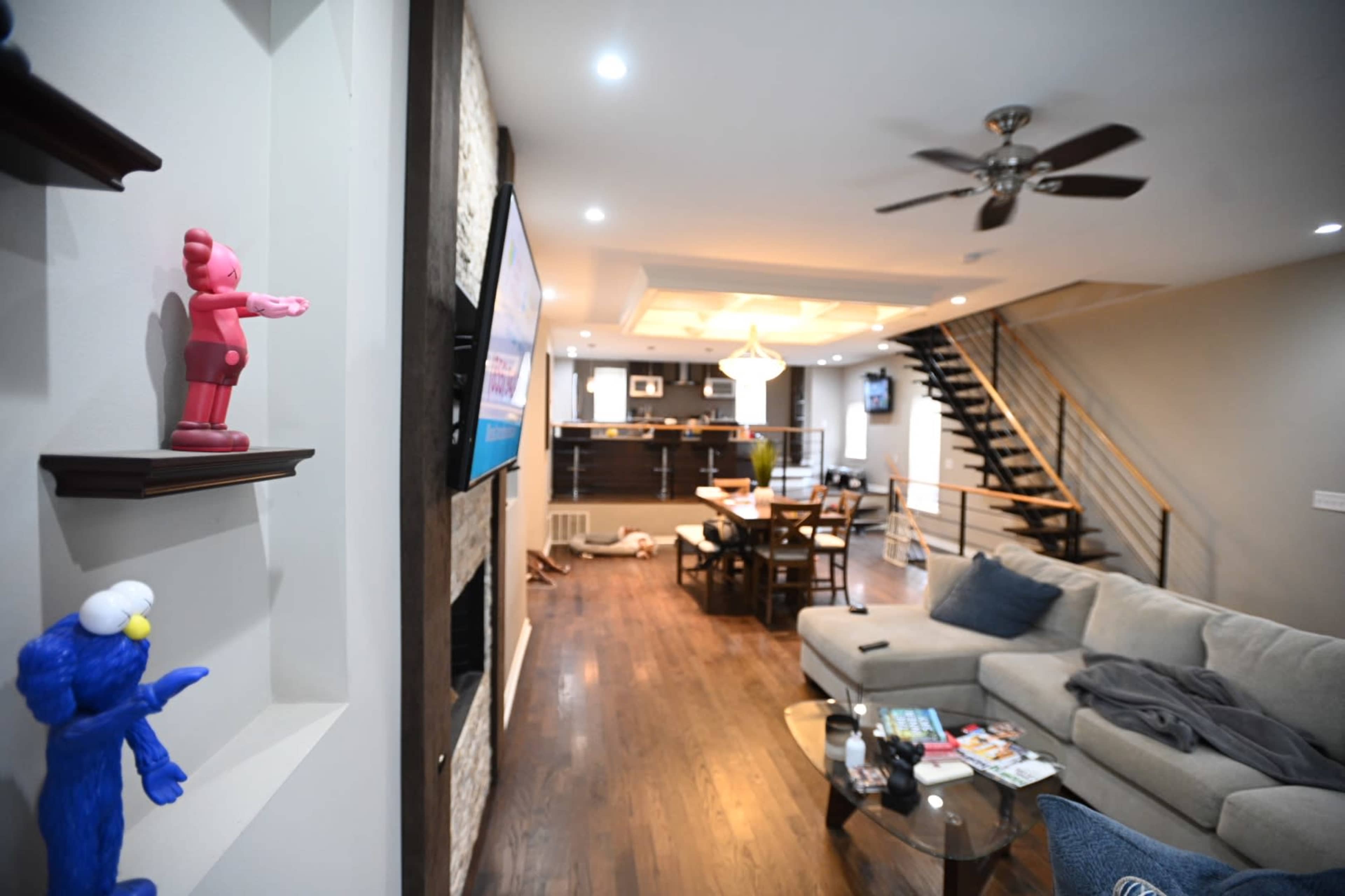 A modern living room with a staircase, a sectional sofa, and a dining area illuminated by ceiling lights.