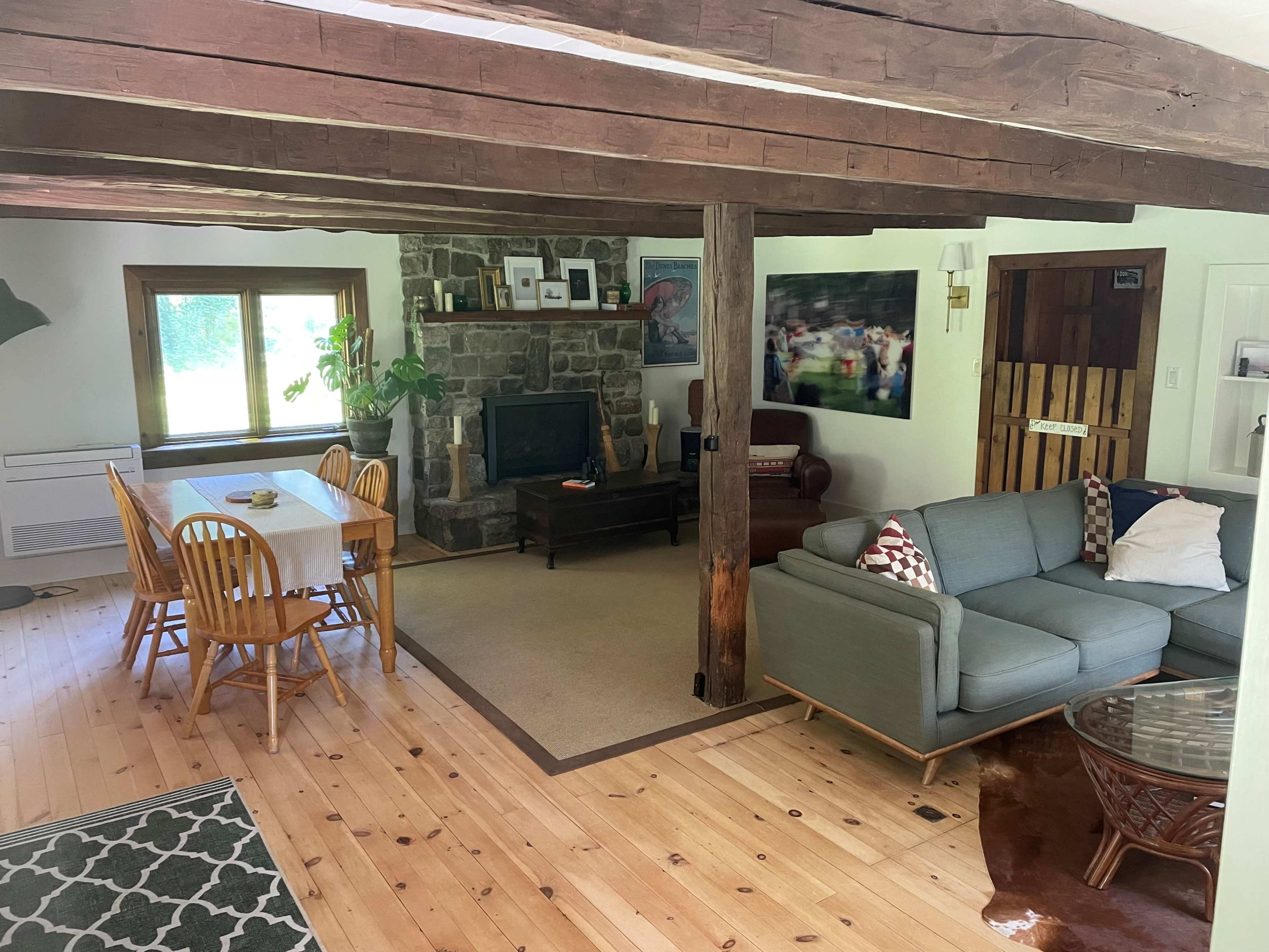 A cozy living space with a stone fireplace, wooden beams, and a mix of dining and seating areas.