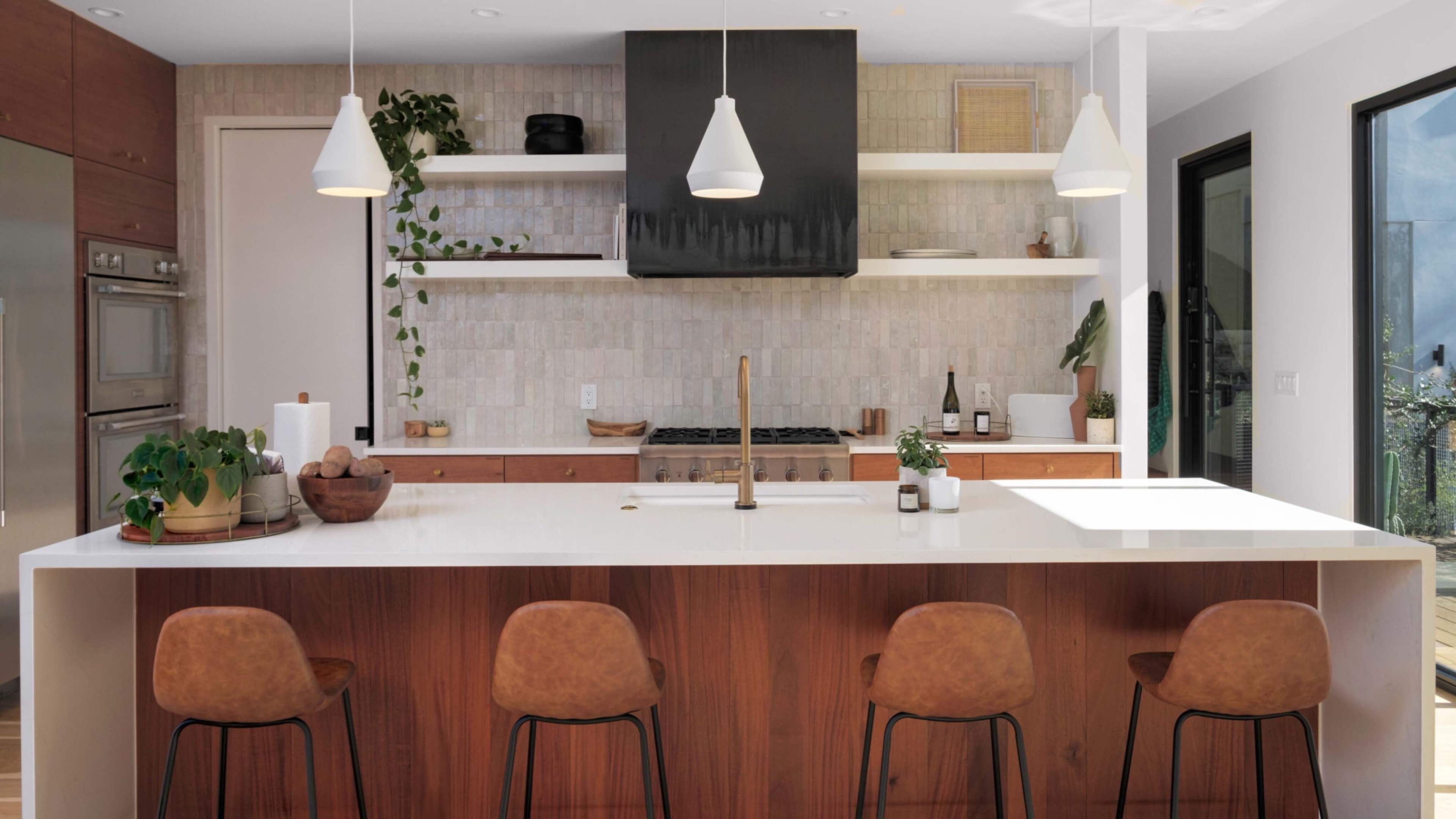 A modern kitchen features a large island with four brown stools, a stainless steel faucet, and open shelving above a wooden countertop.