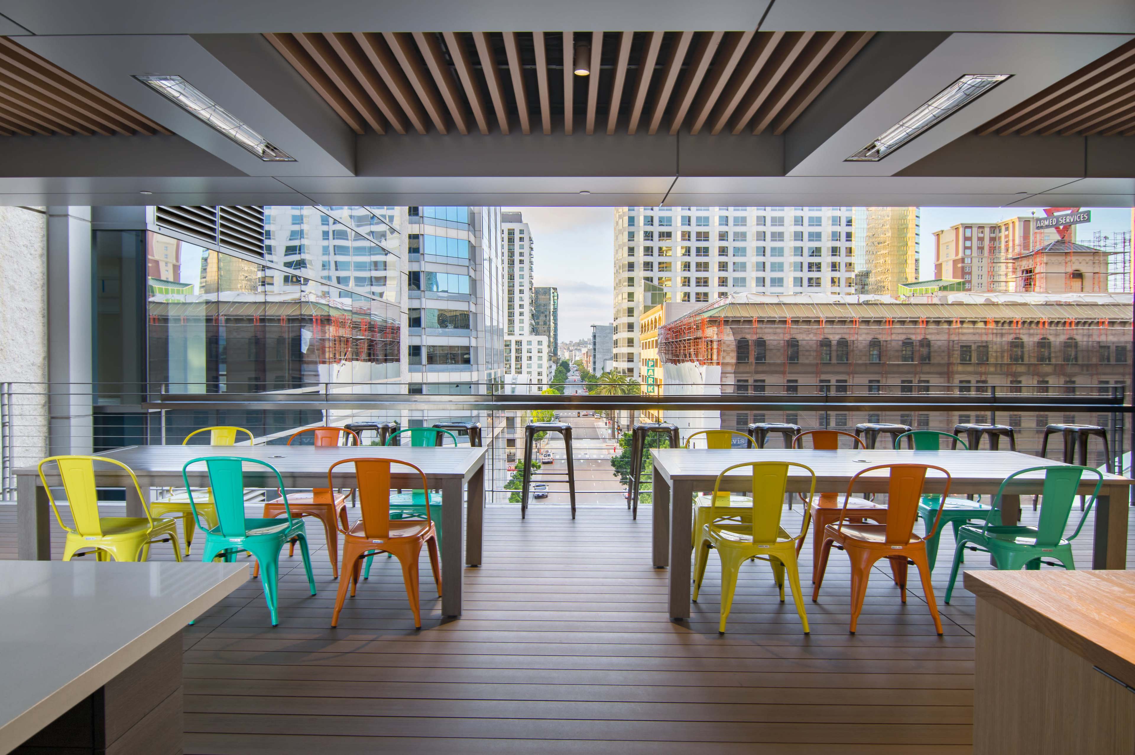 A modern office space features colorful chairs around long tables, with large windows providing a view of the city skyline.