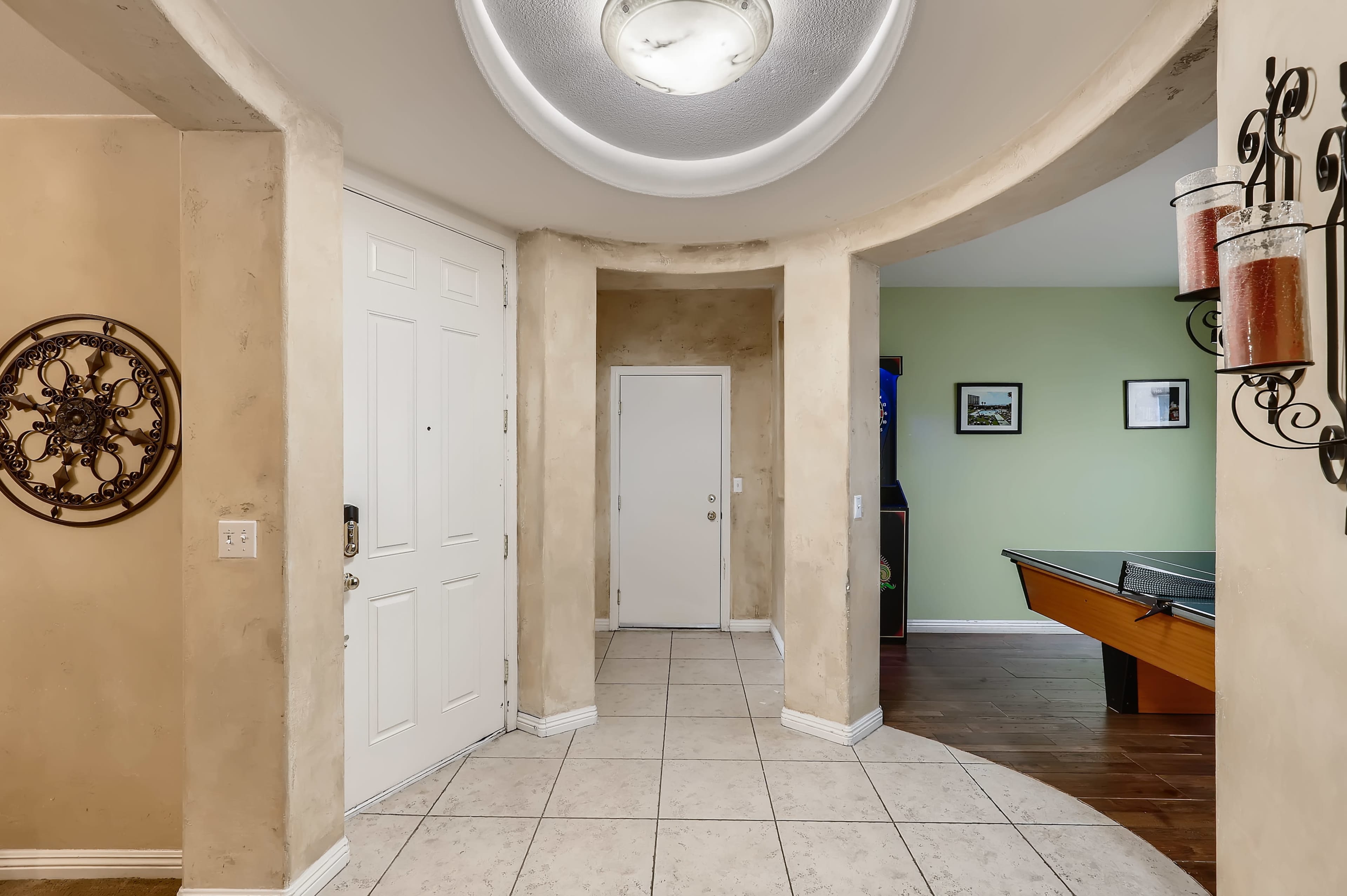 A foyer with a circular archway leading to a hallway, featuring a front door, a small side door, and a view of a game area with a pool table.