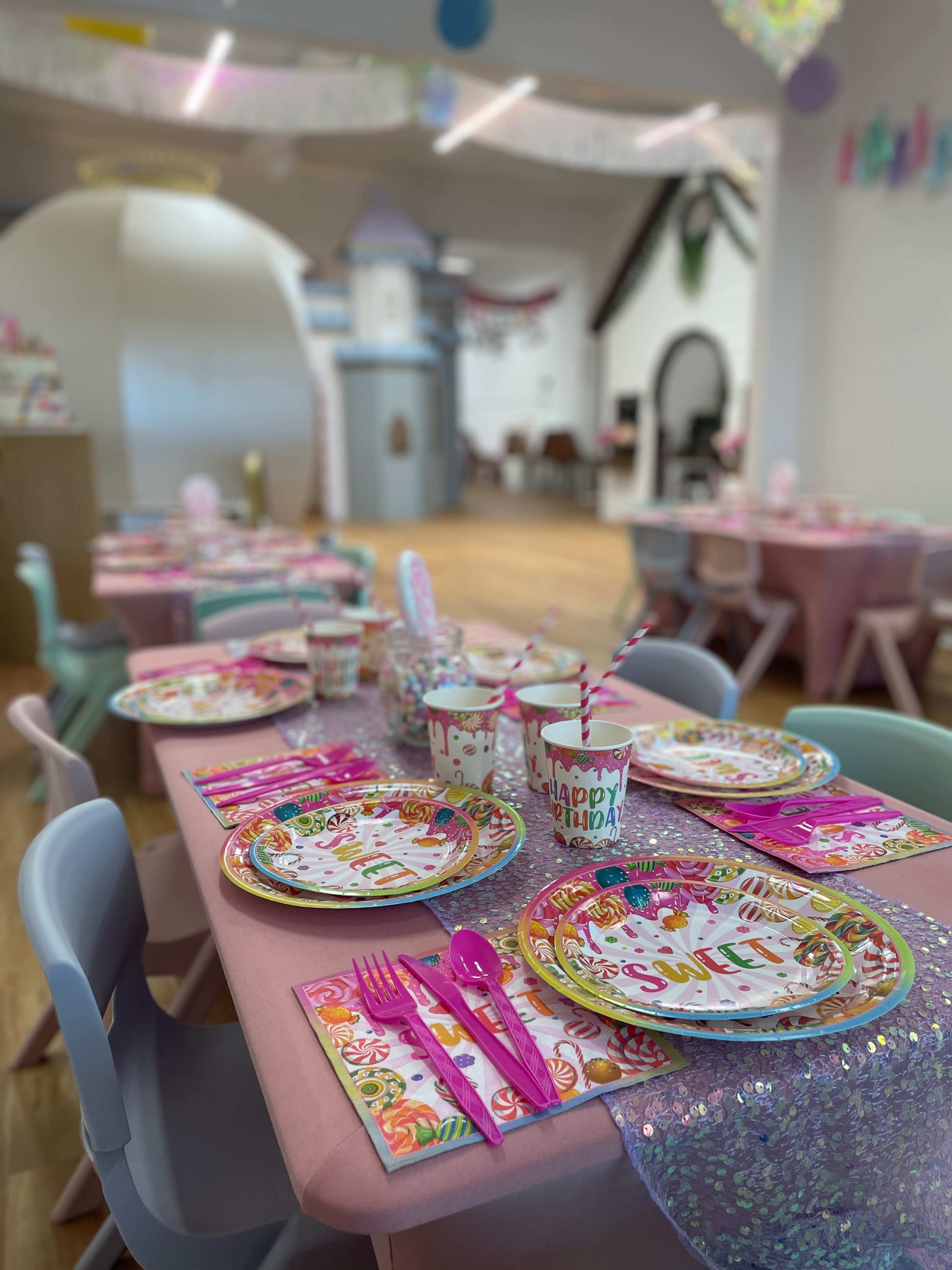 The image shows a decorated party space with tables set for a birthday celebration, featuring colorful plates, cups, and festive decorations.