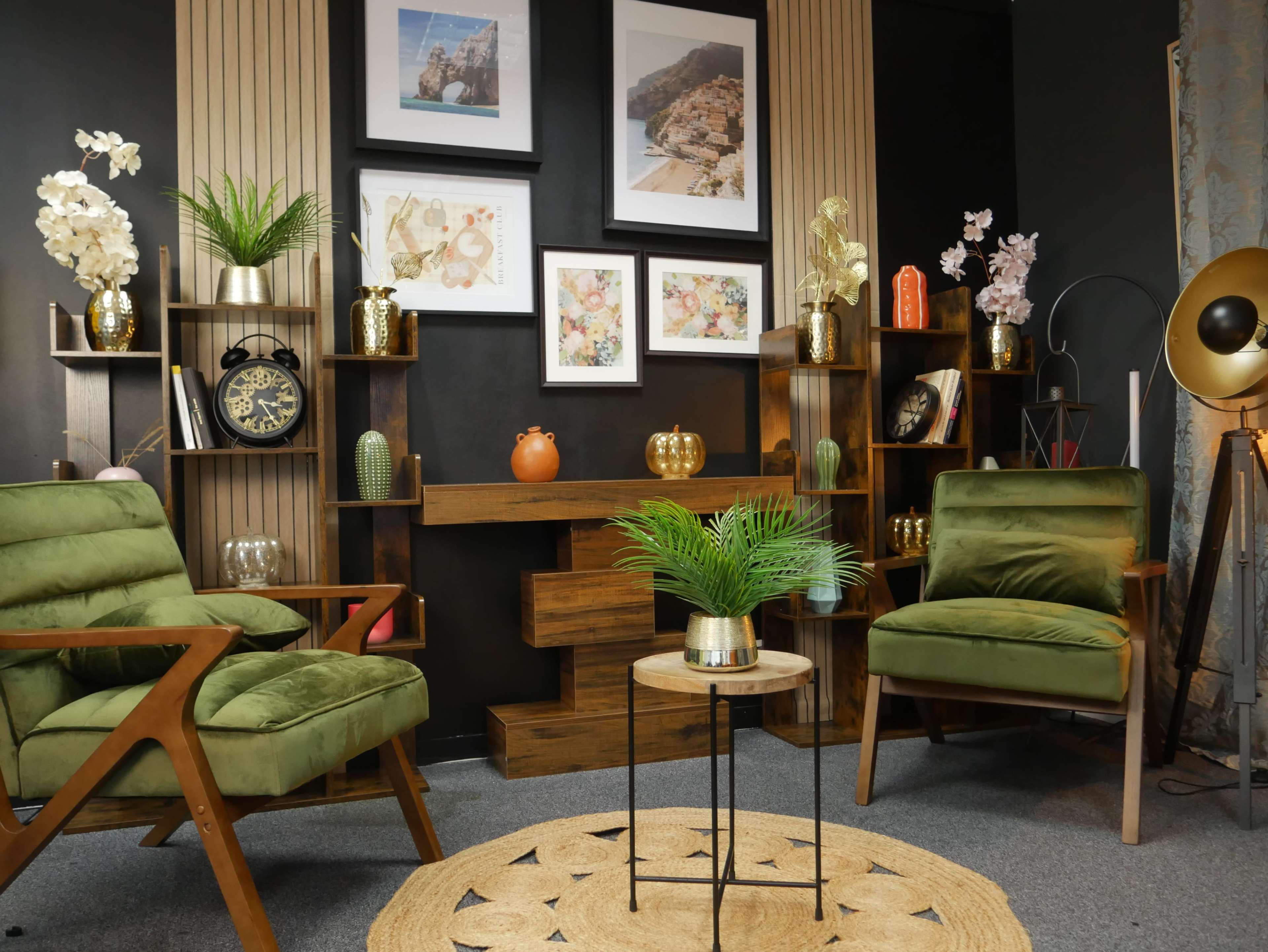 The image shows a stylish interior scene featuring two green armchairs, a small round table, and decorative shelves adorned with plants, vases, and framed artwork.