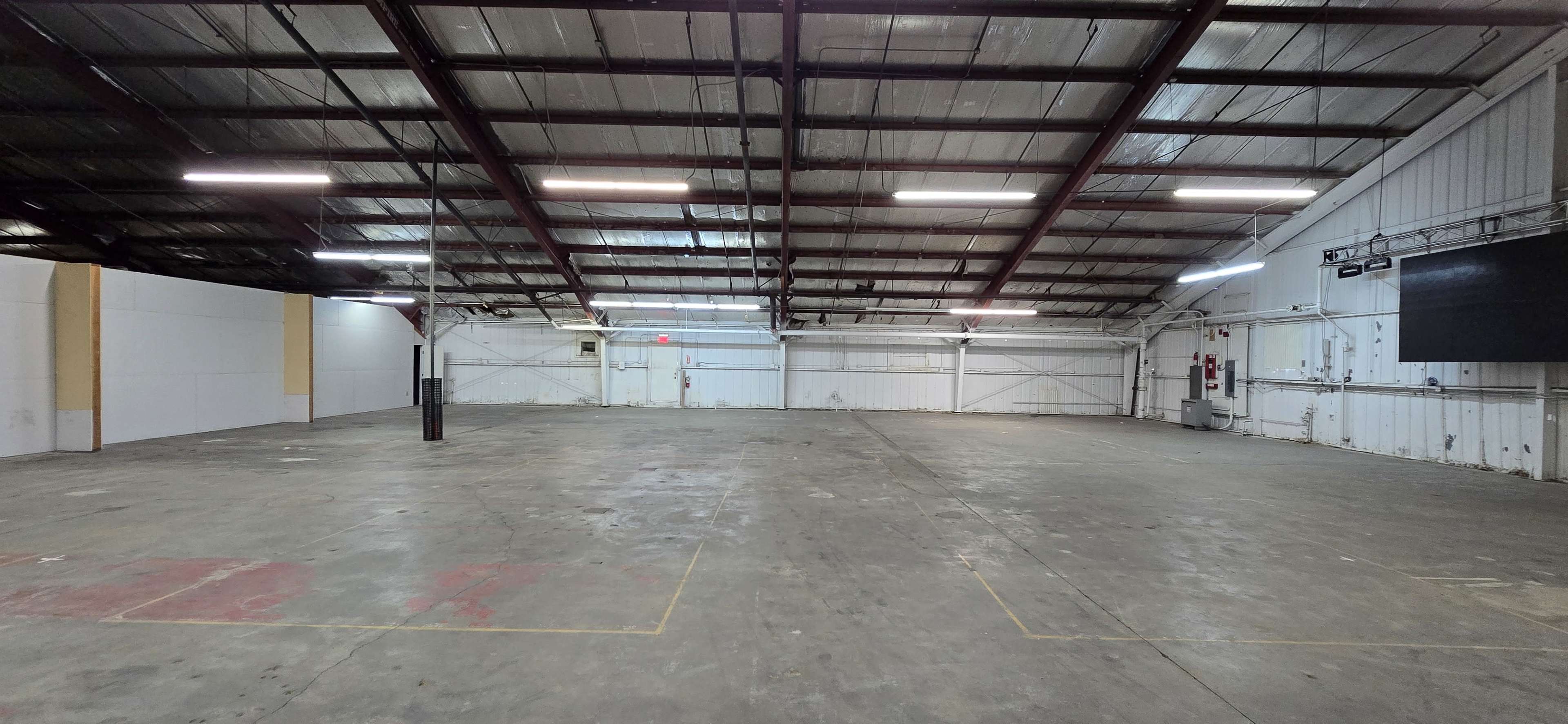 The image shows a large, empty industrial space with a high ceiling, concrete floor, and minimal wall features.