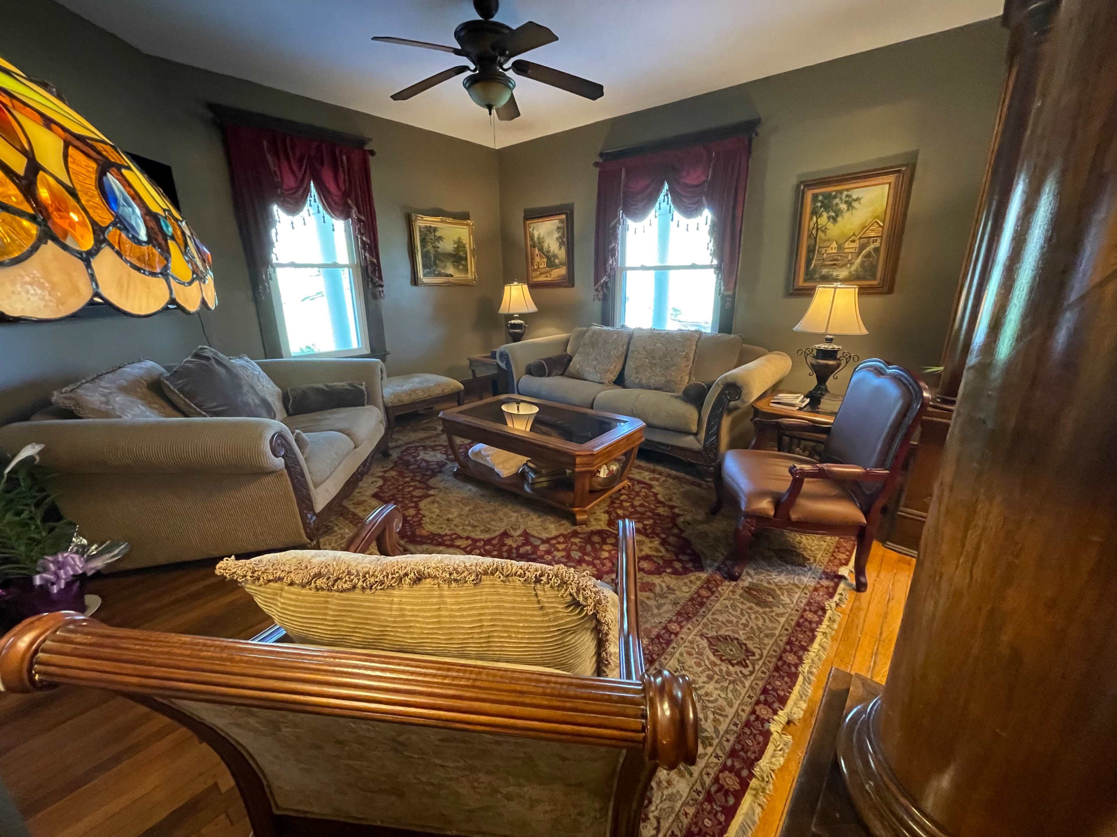 A cozy living room with a couch, armchairs, and a wooden coffee table, adorned with framed artwork and a stained glass lamp.