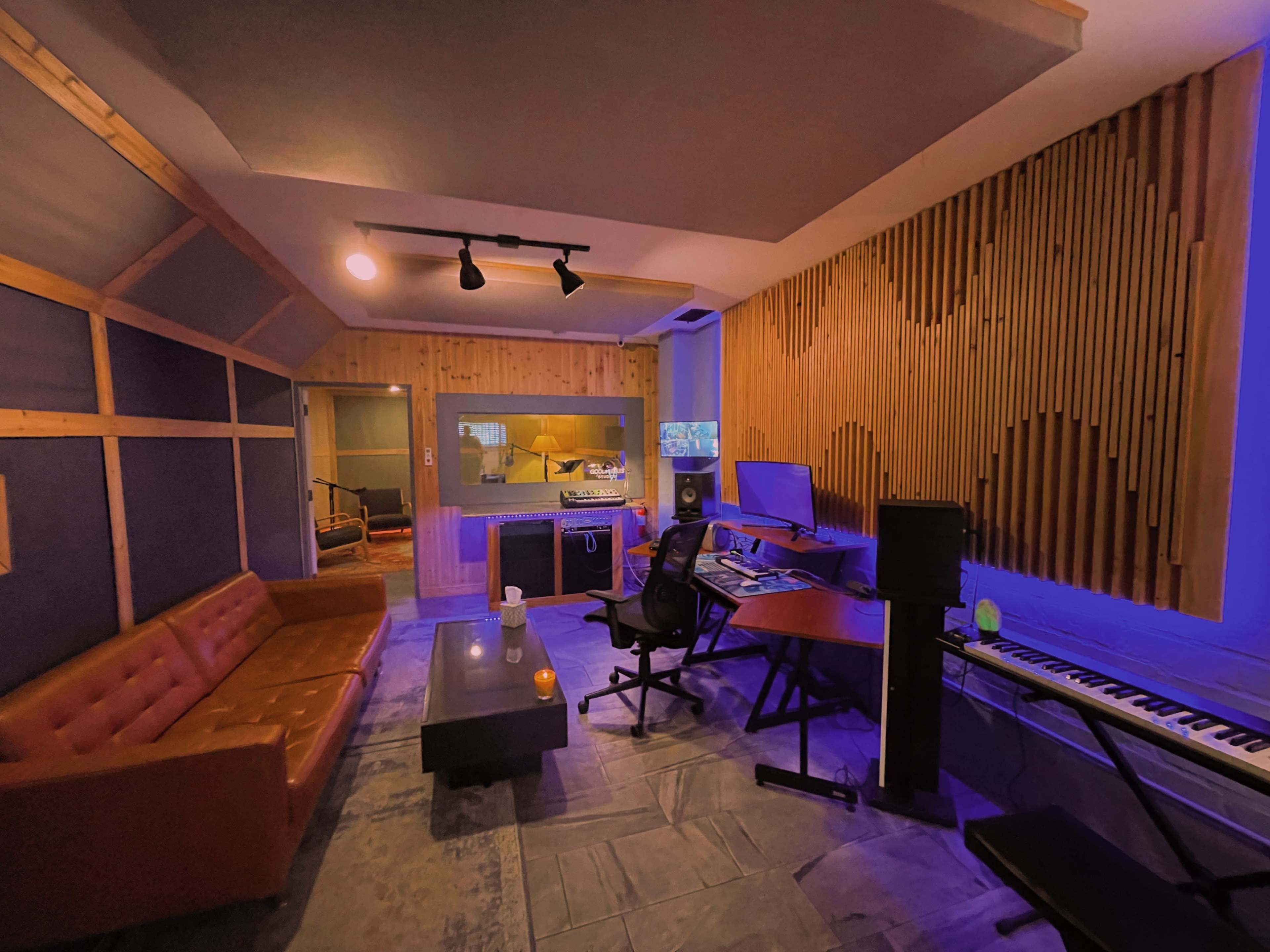 A recording studio with wooden paneling, a keyboard, a desk, and a seating area that includes an orange couch.