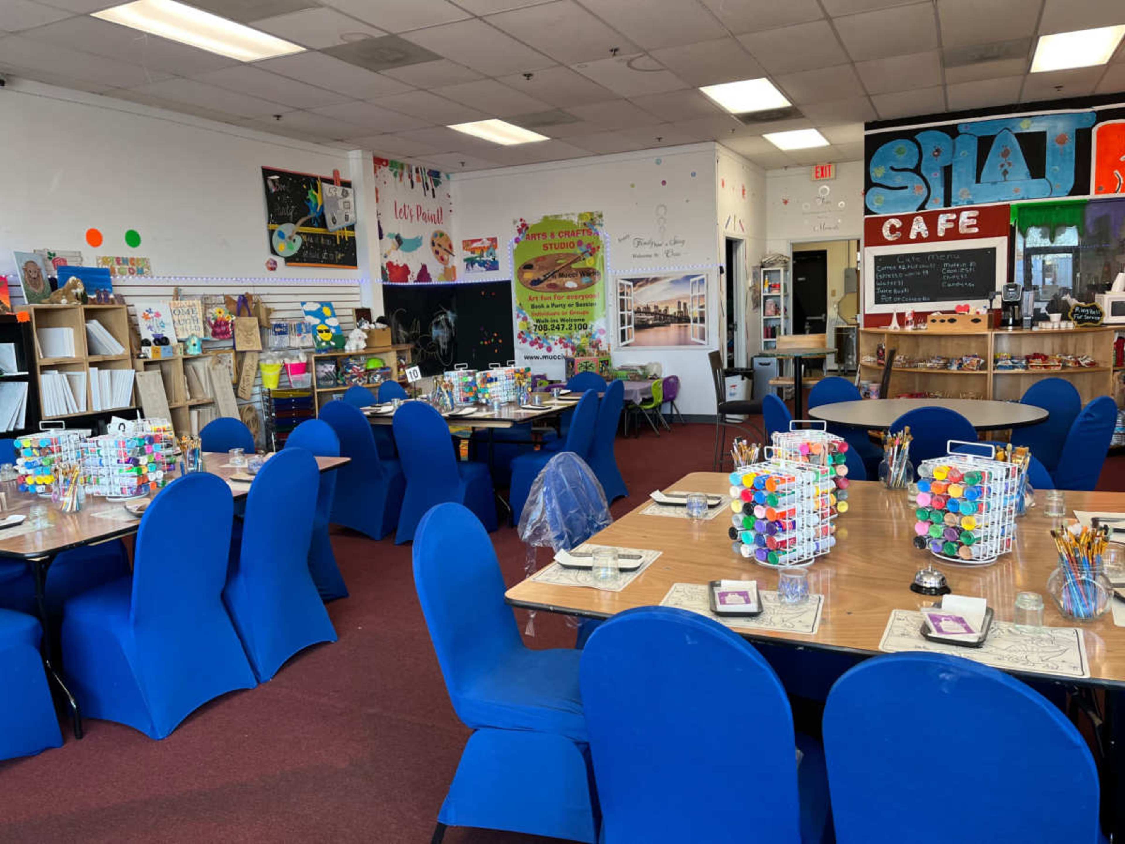 A vibrant art studio with several tables set up for painting and crafting, surrounded by colorful artwork and supplies.