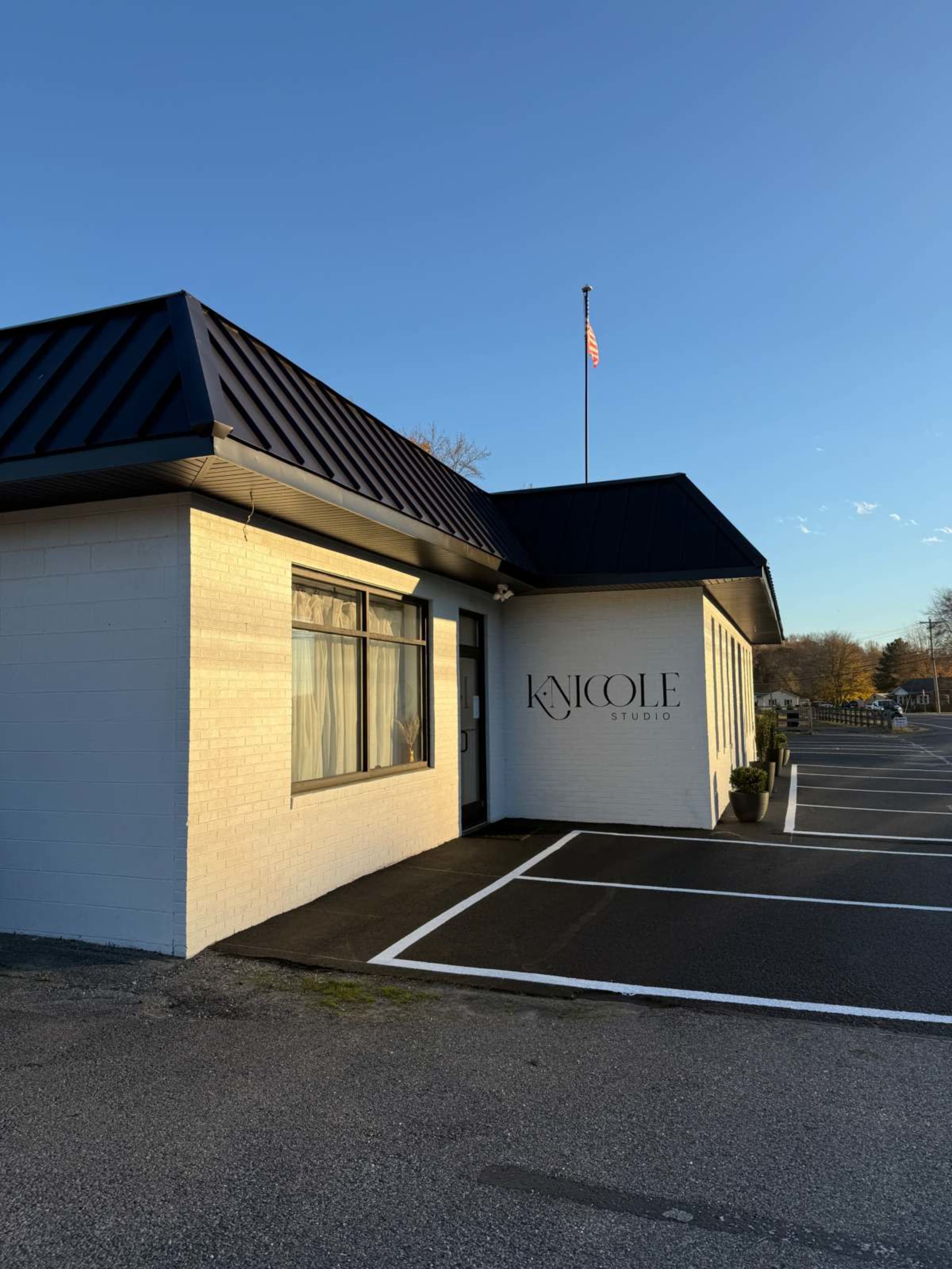 The image shows a building with a white exterior and a dark roof, featuring the sign "KNicole Studio" on the side, along with an American flag flying above.