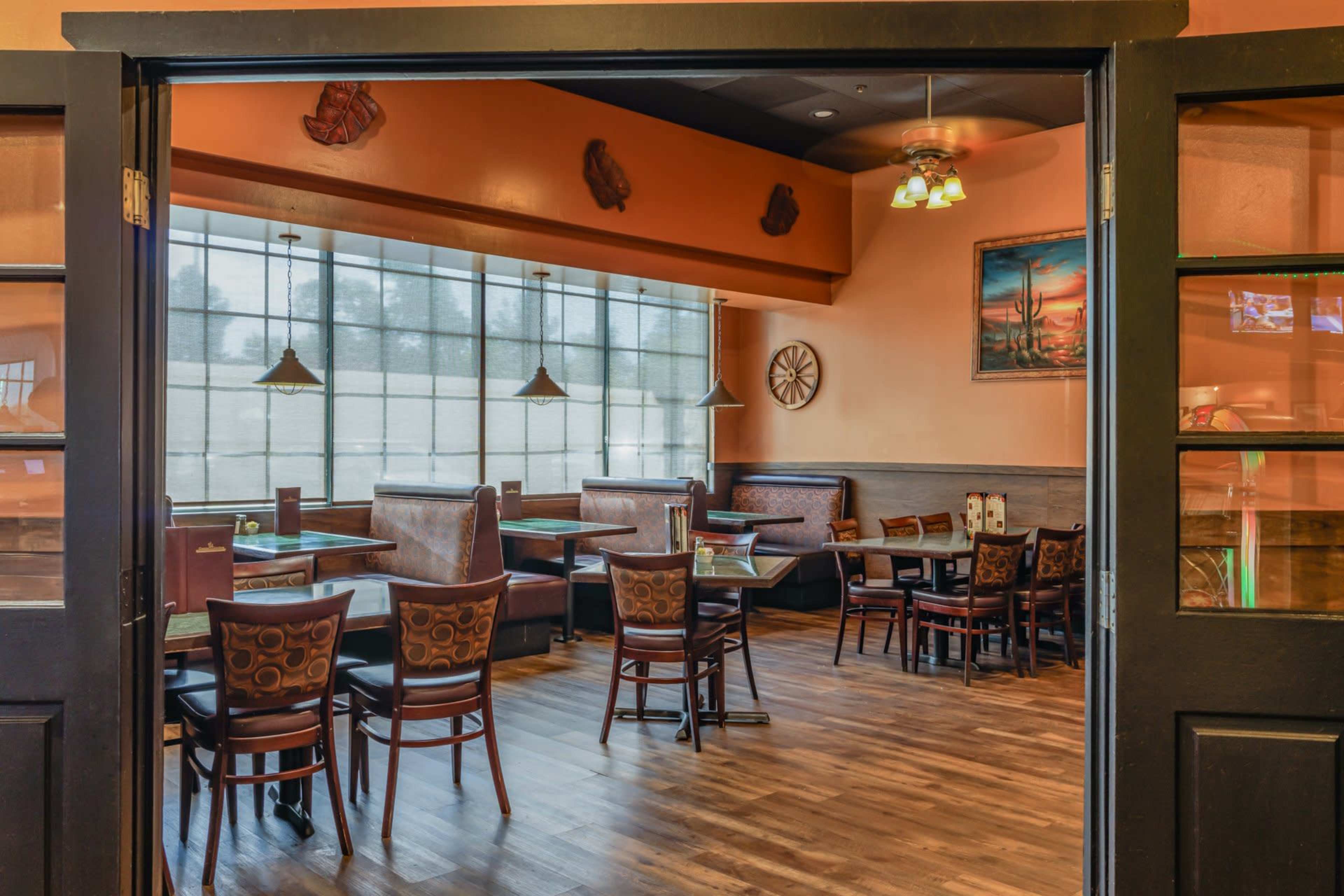 The image shows an empty restaurant interior with wooden floors, orange walls, and tables set for dining.