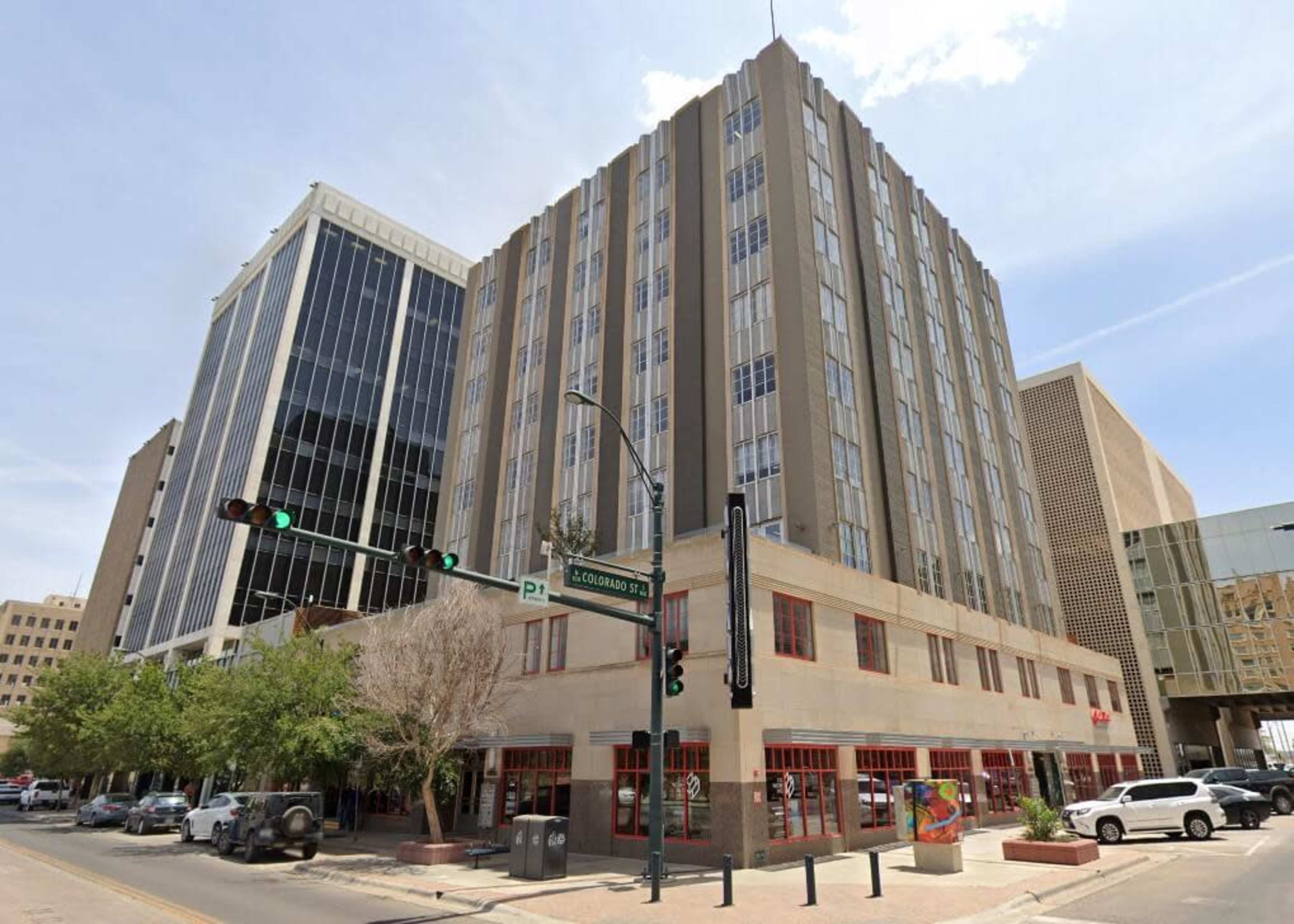 A city intersection with several buildings, including a tall glass skyscraper and a mid-rise structure featuring a detailed facade.
