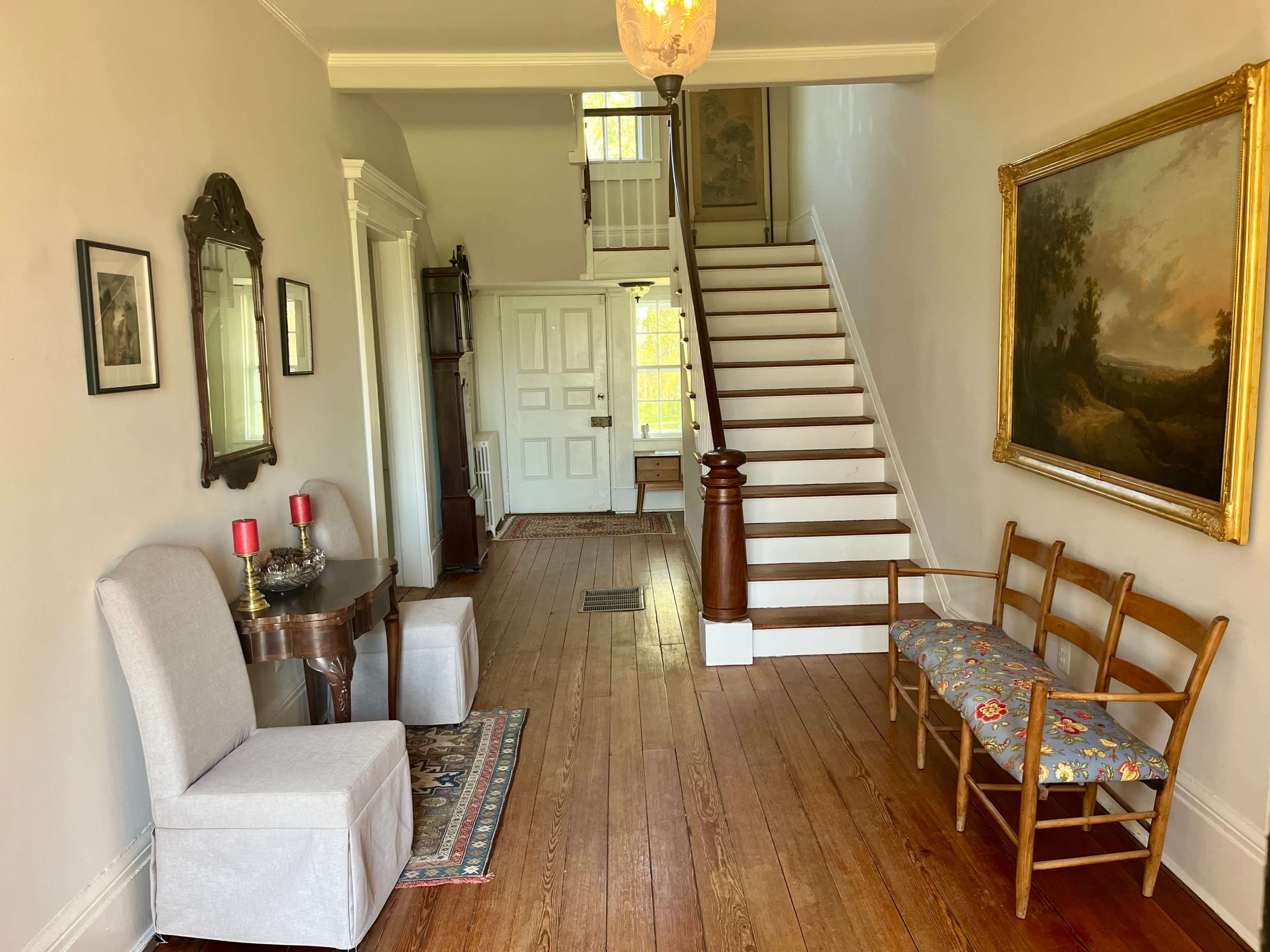 A foyer with a staircase, a seating area with a floral bench, and a table with two candles.