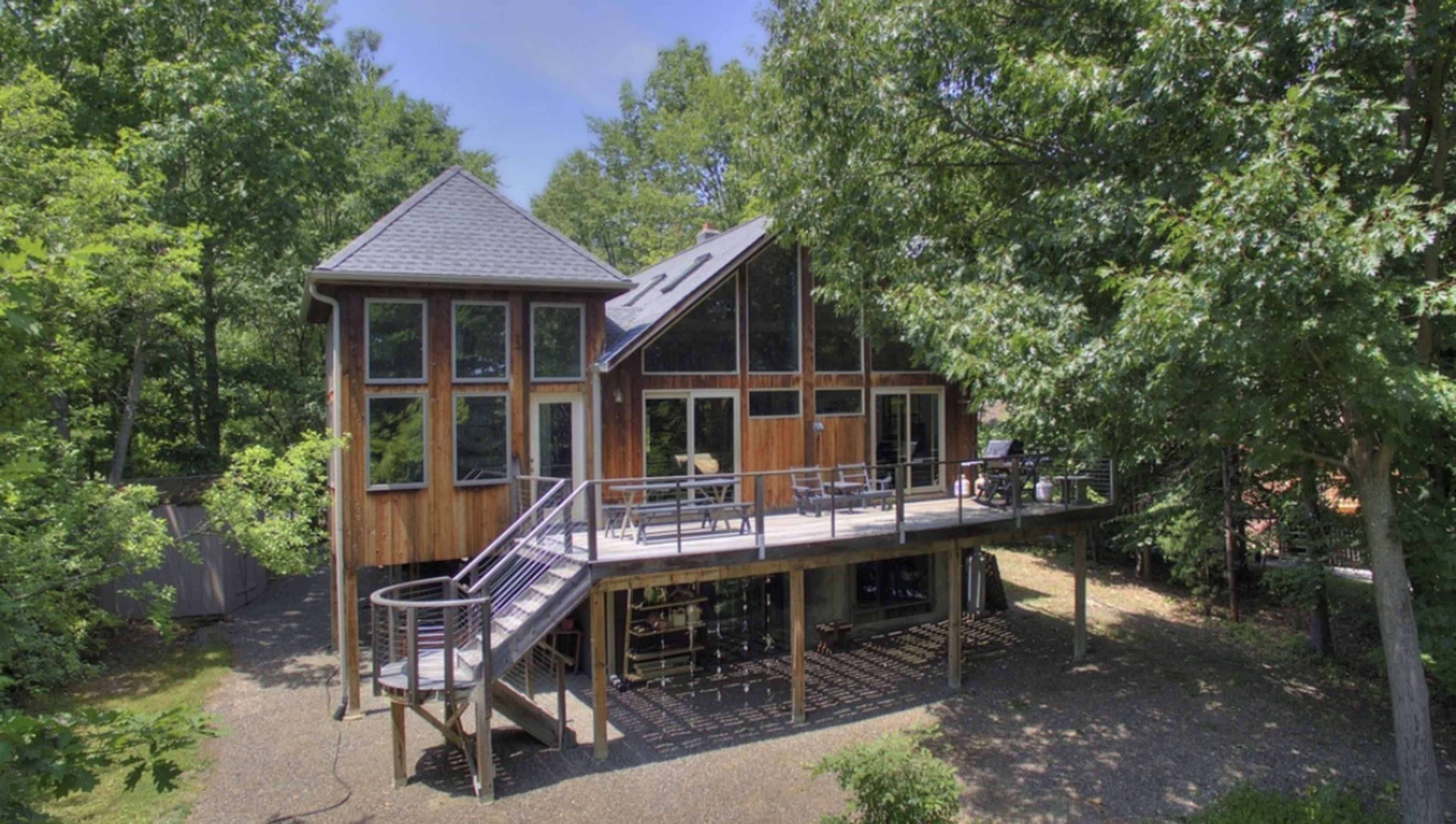 A wooden house with large windows and a wraparound deck is situated among trees.