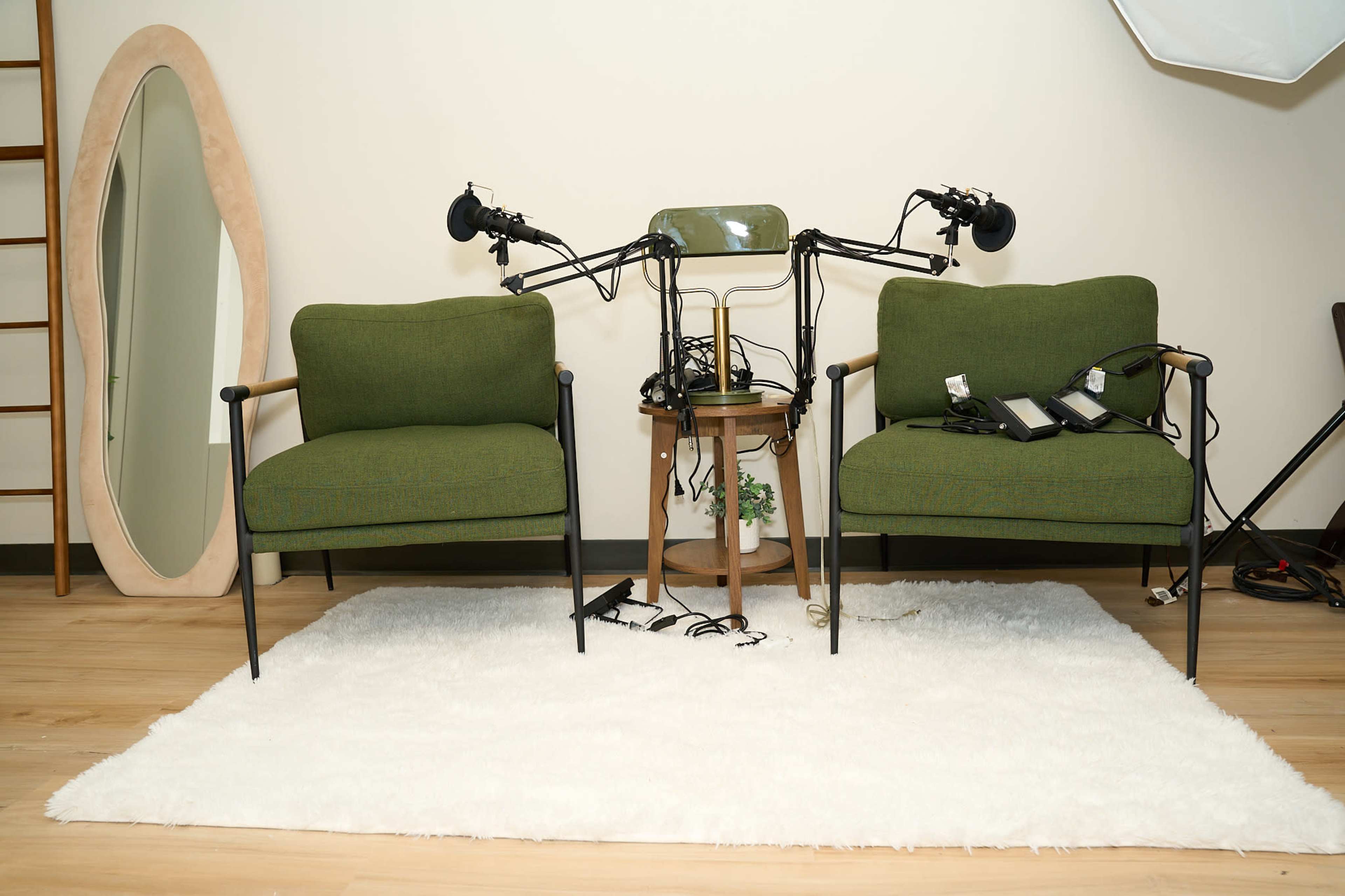 The image shows two green chairs on a white rug, with a small table between them displaying tangled wires and microphones.