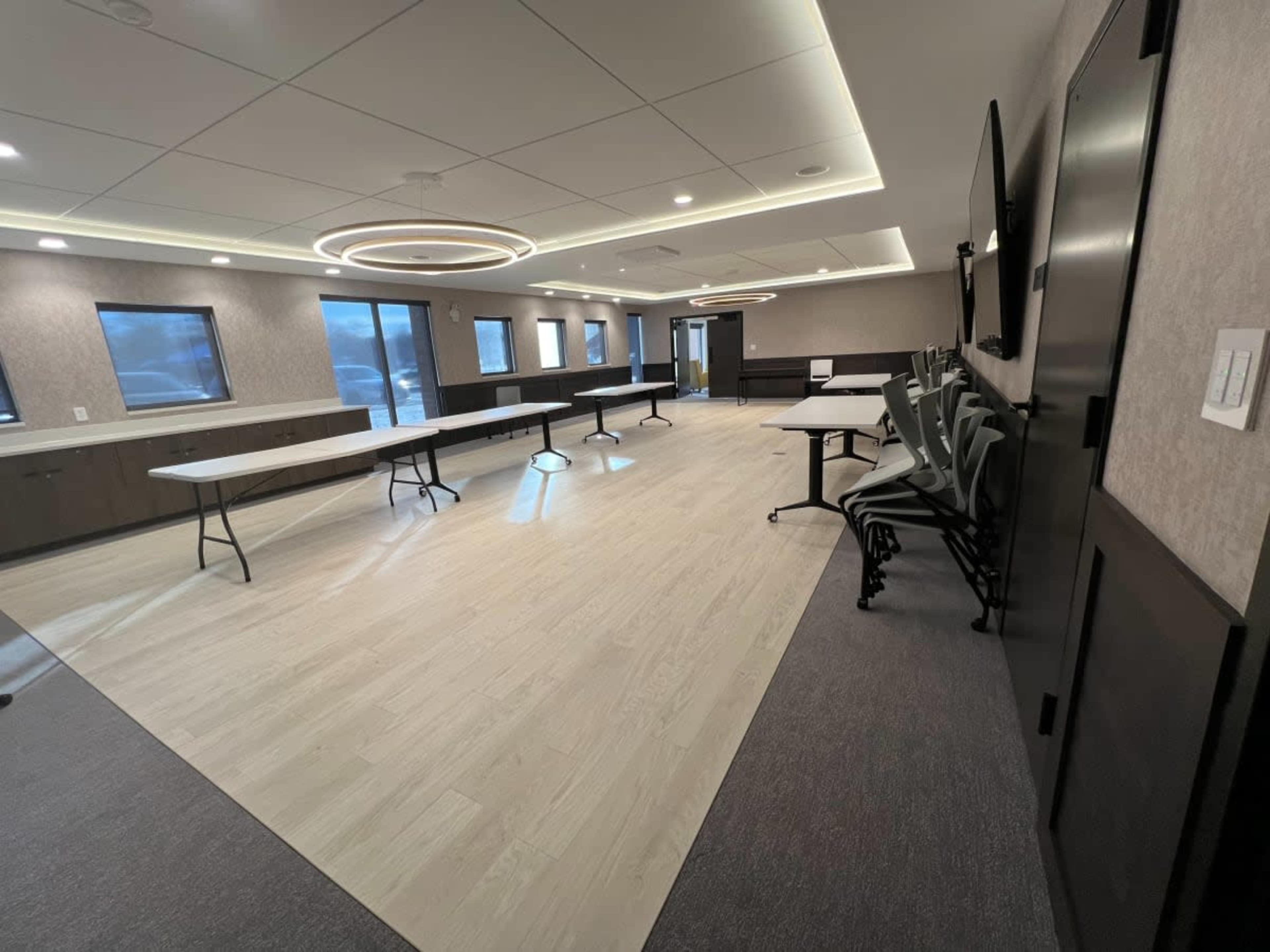 An empty conference room with several tables arranged in rows and chairs stacked against the wall.