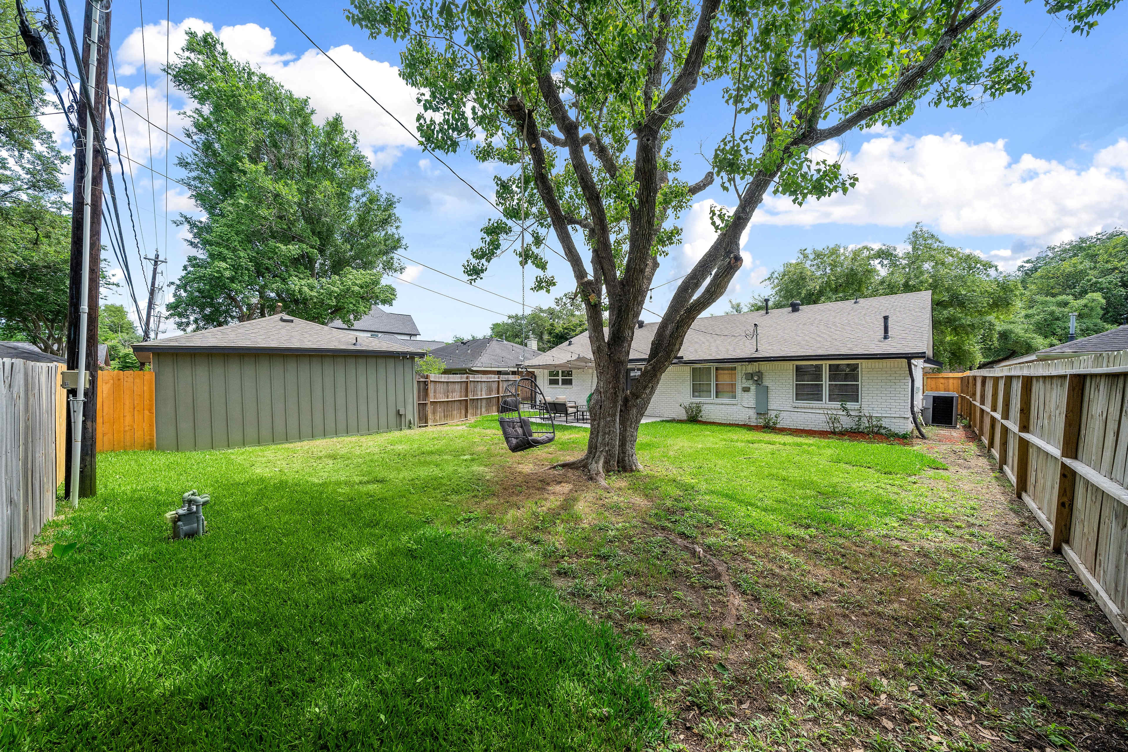 A spacious backyard with a tree, a swing, and a fence surrounding the property, along with a nearby shed.
