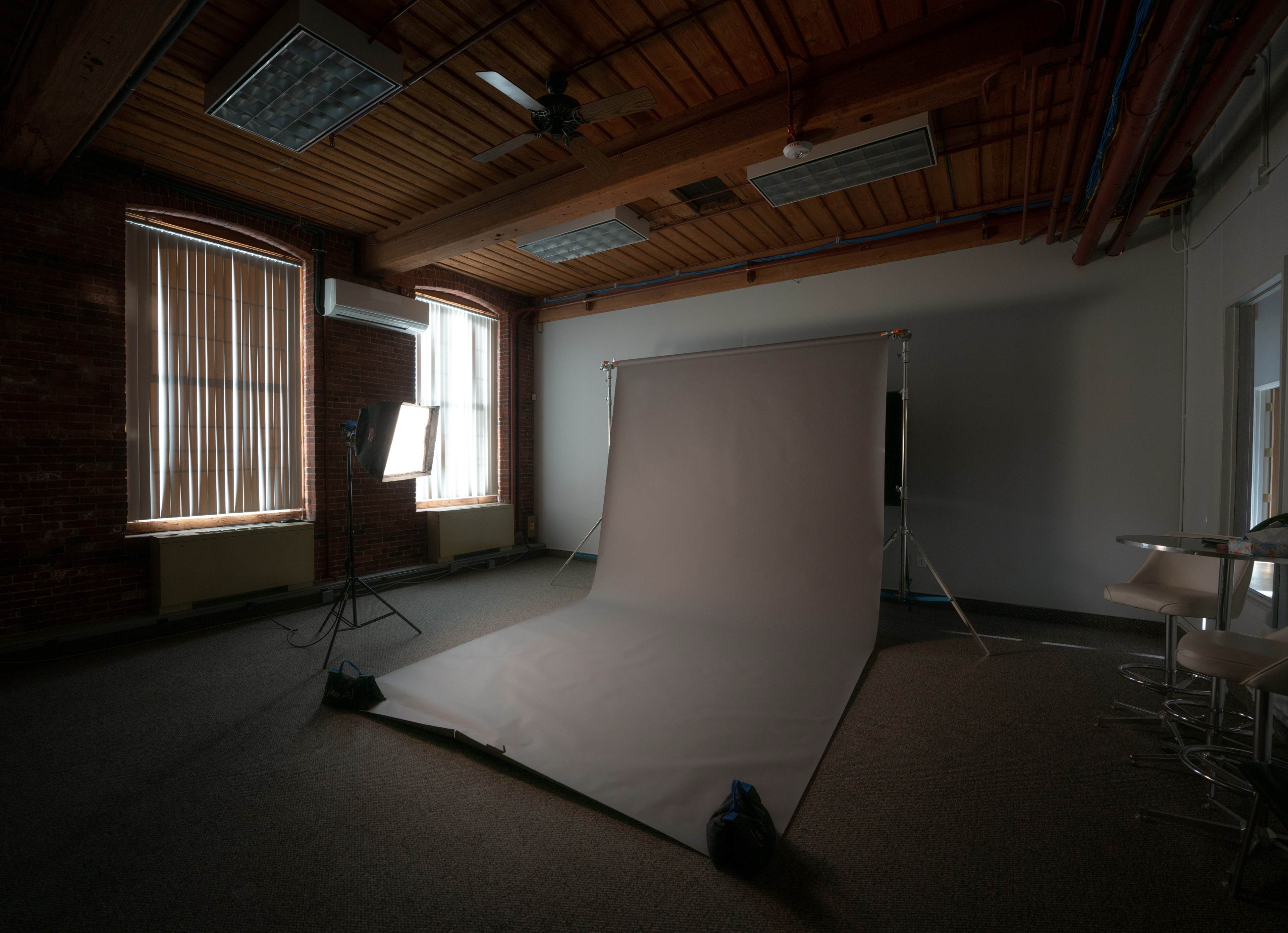 A photography studio features a backdrop setup with a large gray sheet and lighting equipment in a room with exposed brick walls and large windows.