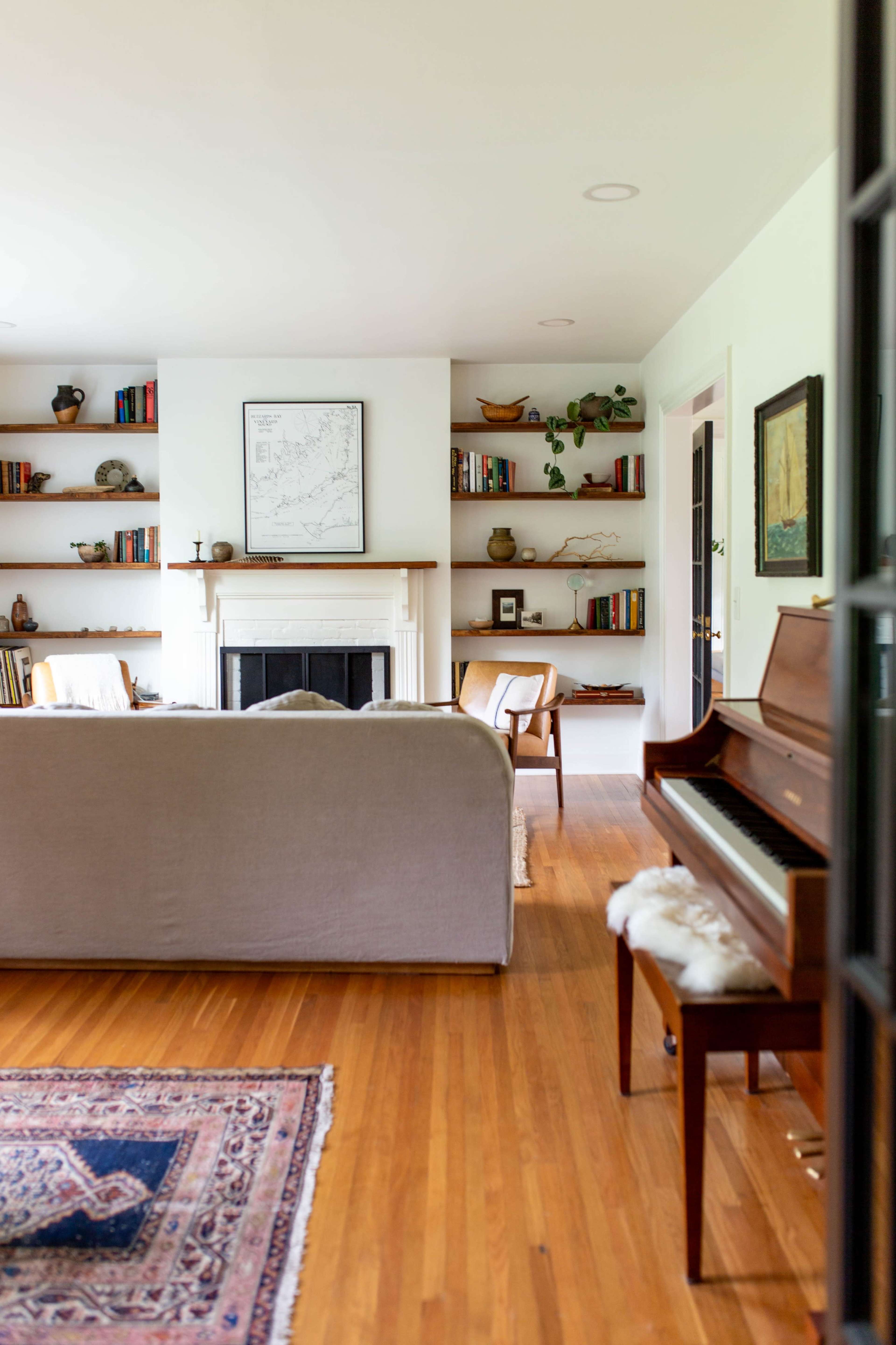 A cozy living room features a fireplace with shelves of books and decorative items, a sofa, and a piano.