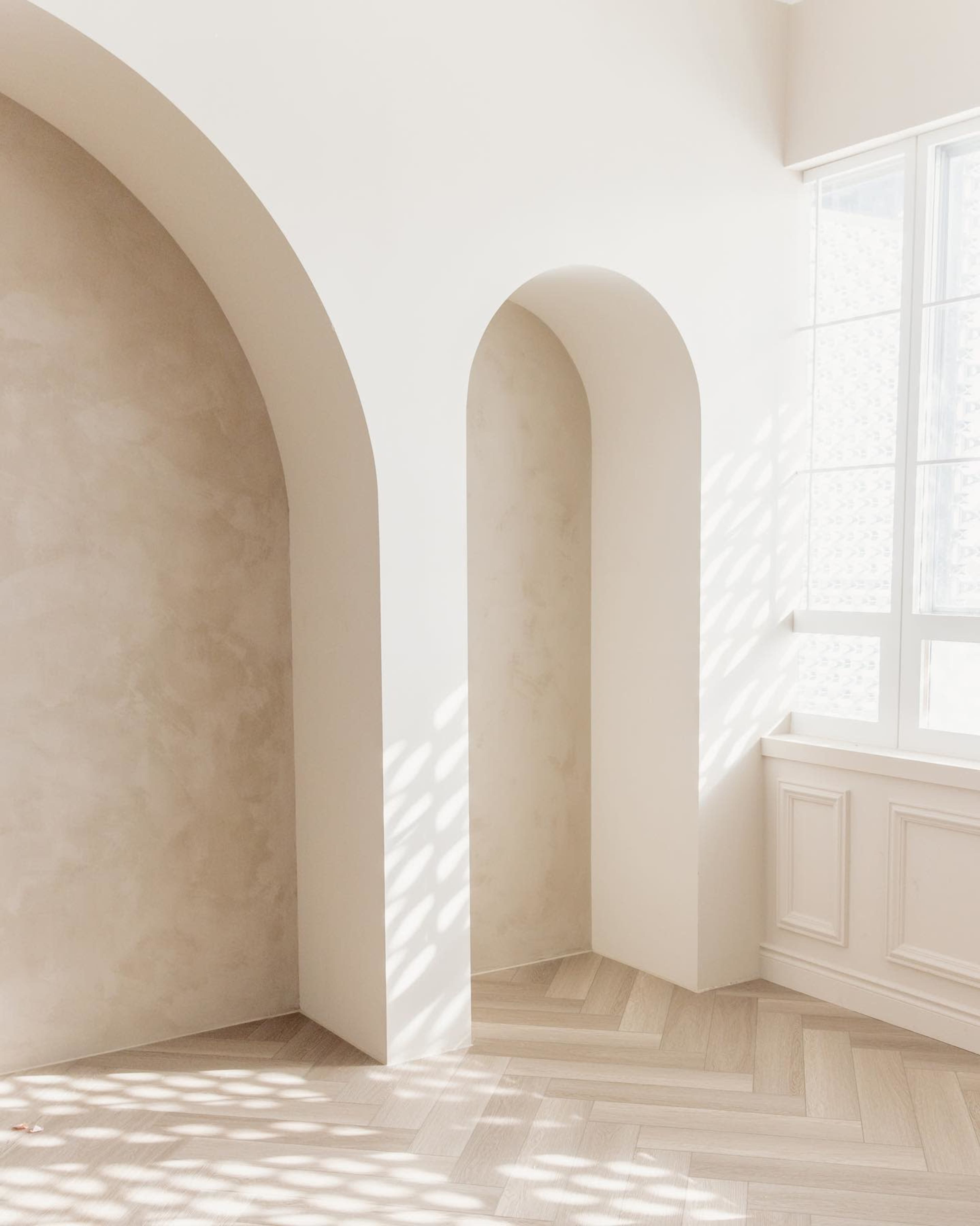 A minimalist interior with arched walls and soft natural light streaming in through a window.