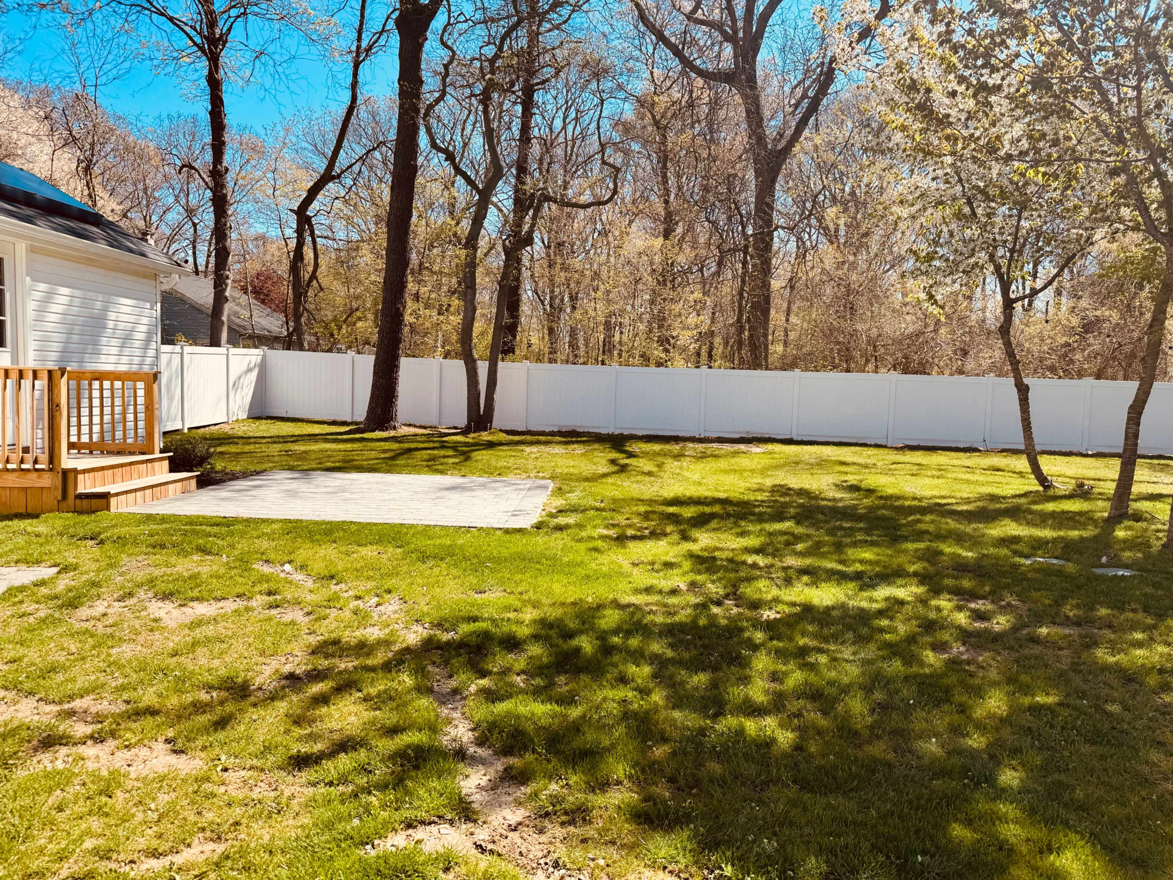 A well-maintained grassy yard bordered by a white fence and shaded by several trees.