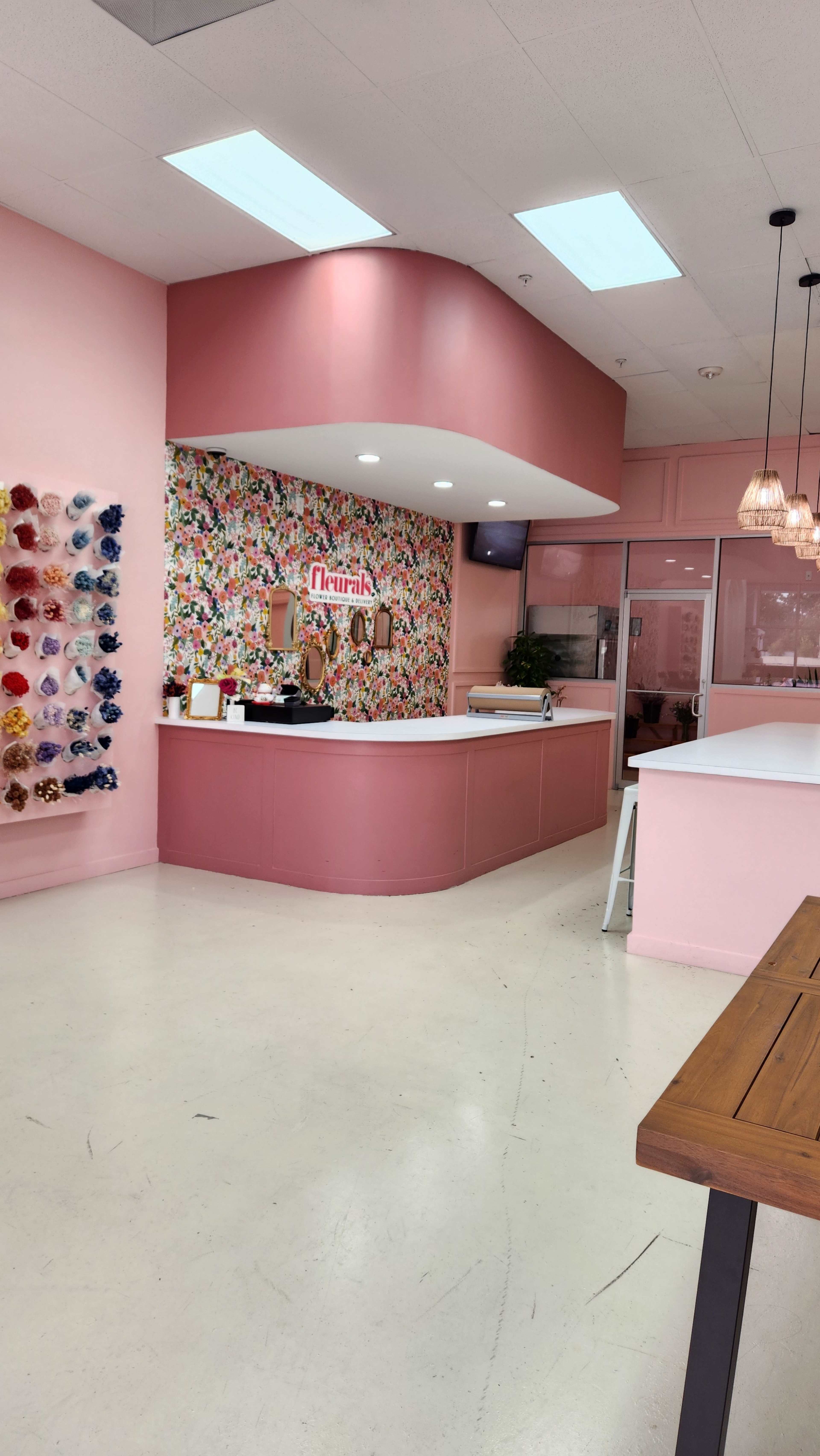 A brightly colored interior of a beauty salon with pink walls, floral wallpaper, and a reception counter.