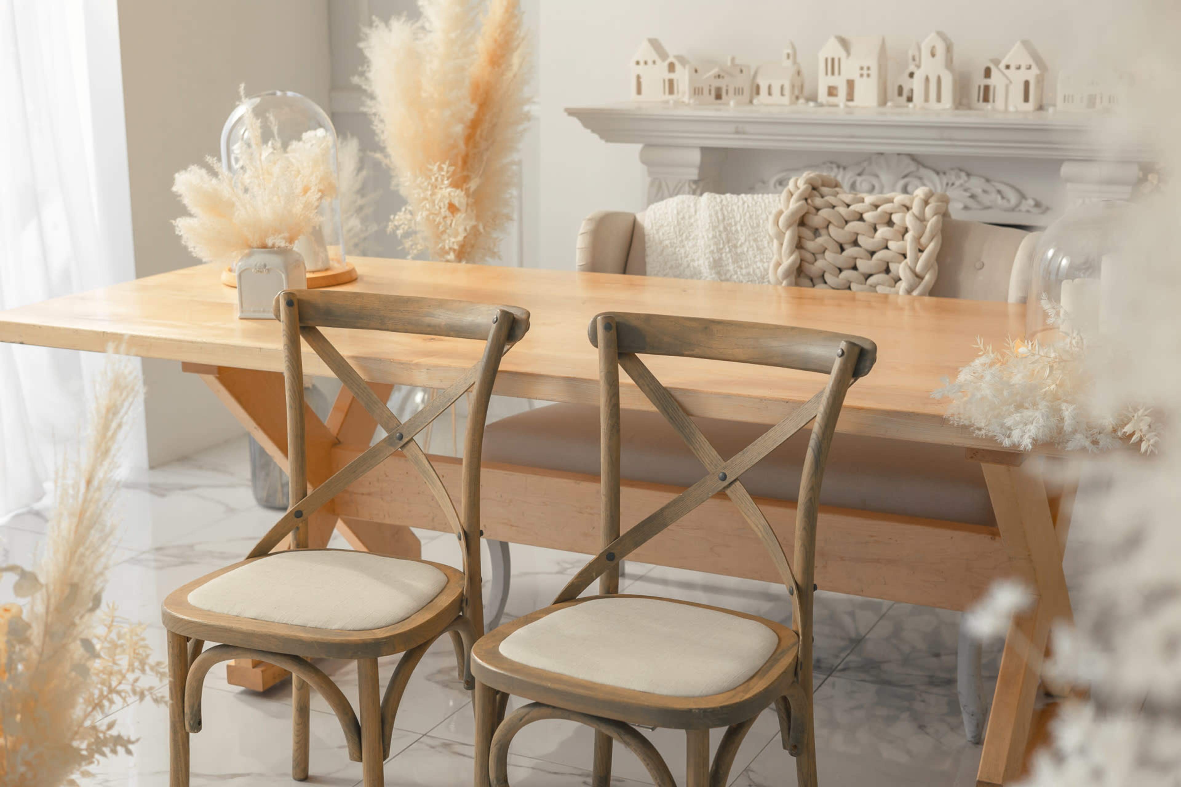 A wooden dining table with two chairs sits in a bright room adorned with decorative items and dried plants.