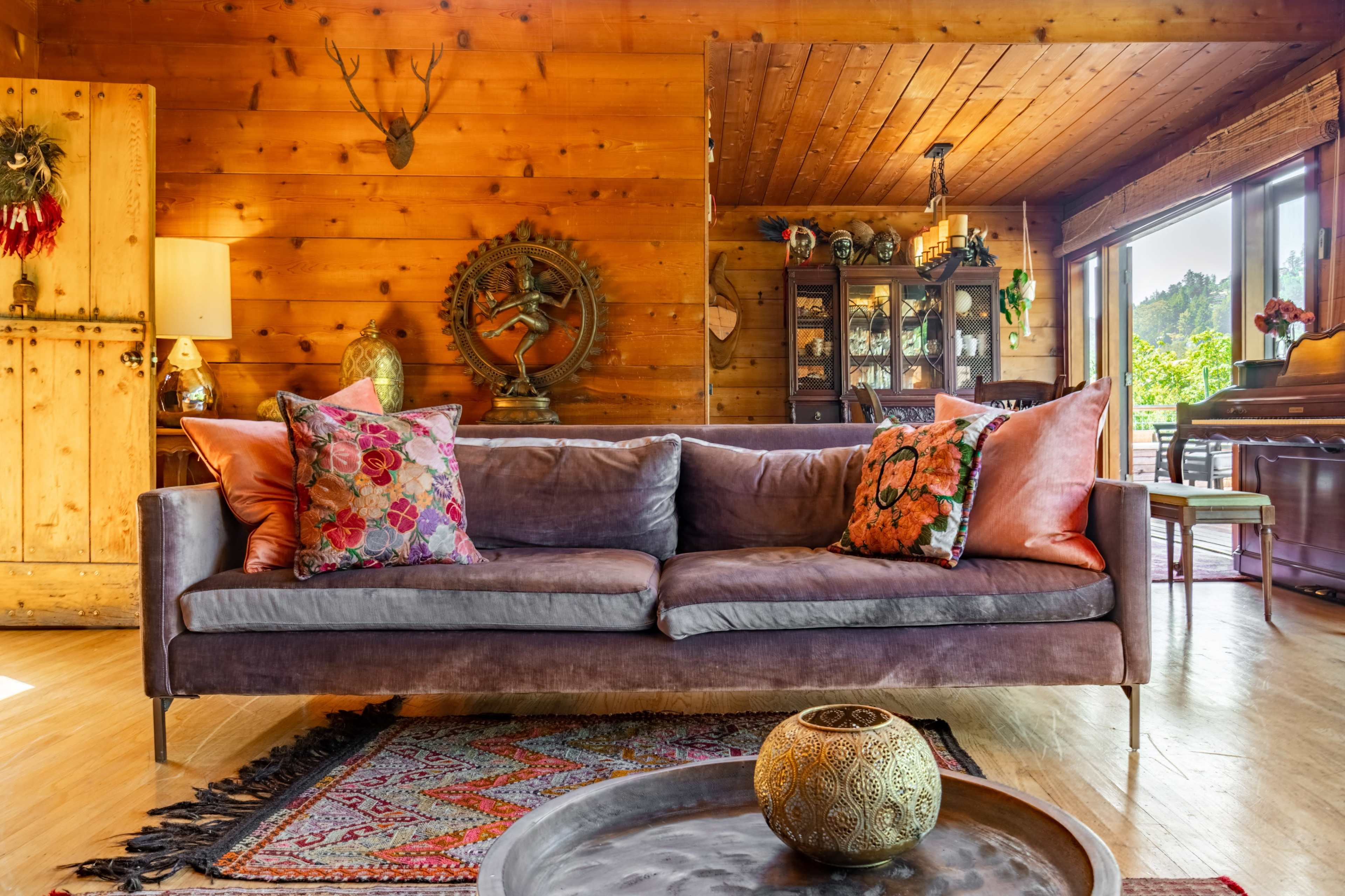 A cozy living room features a plush sofa with colorful pillows, a patterned rug, and wooden walls adorned with decorative items.