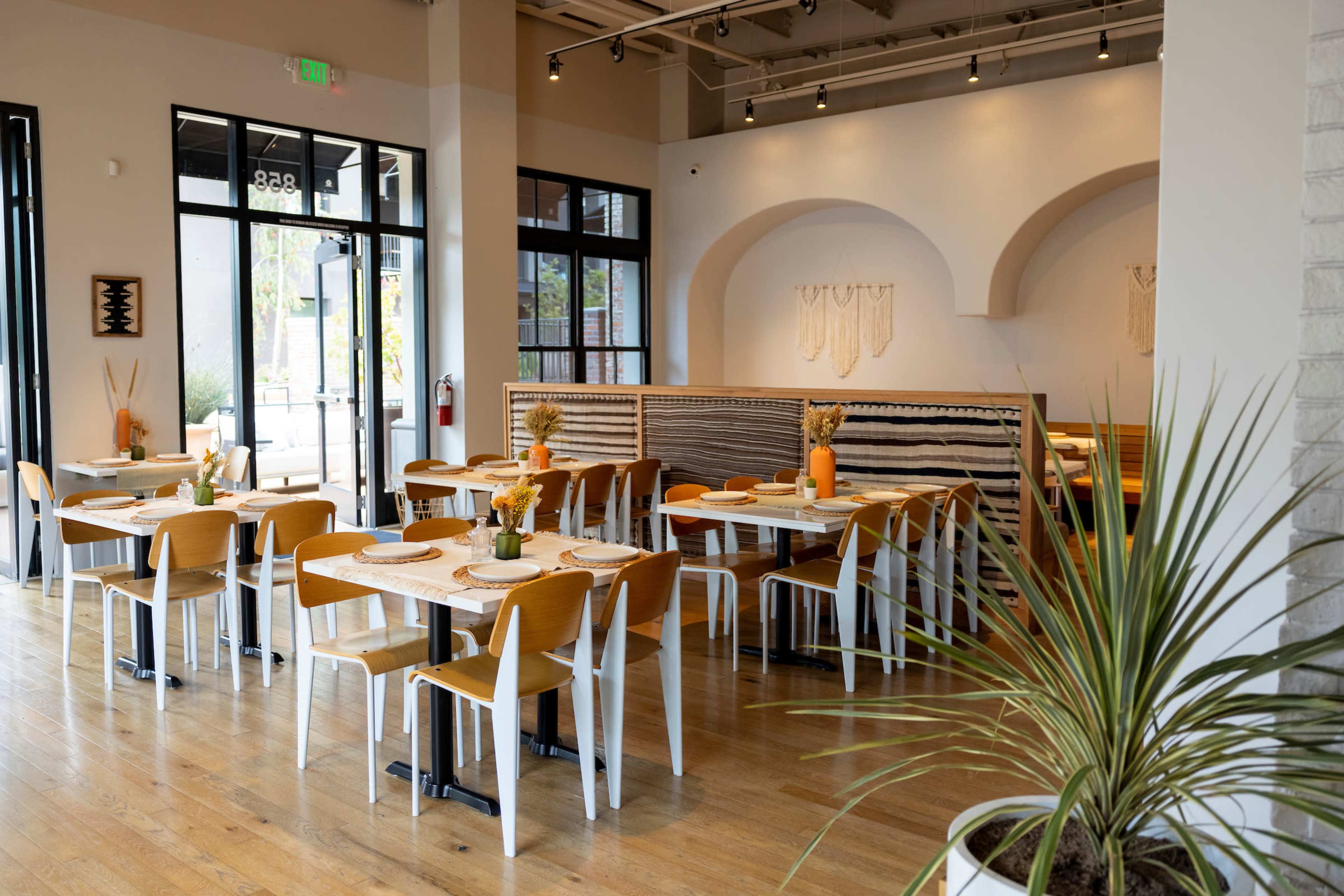 A modern restaurant interior with wooden tables and chairs, large windows, and decorative wall art.