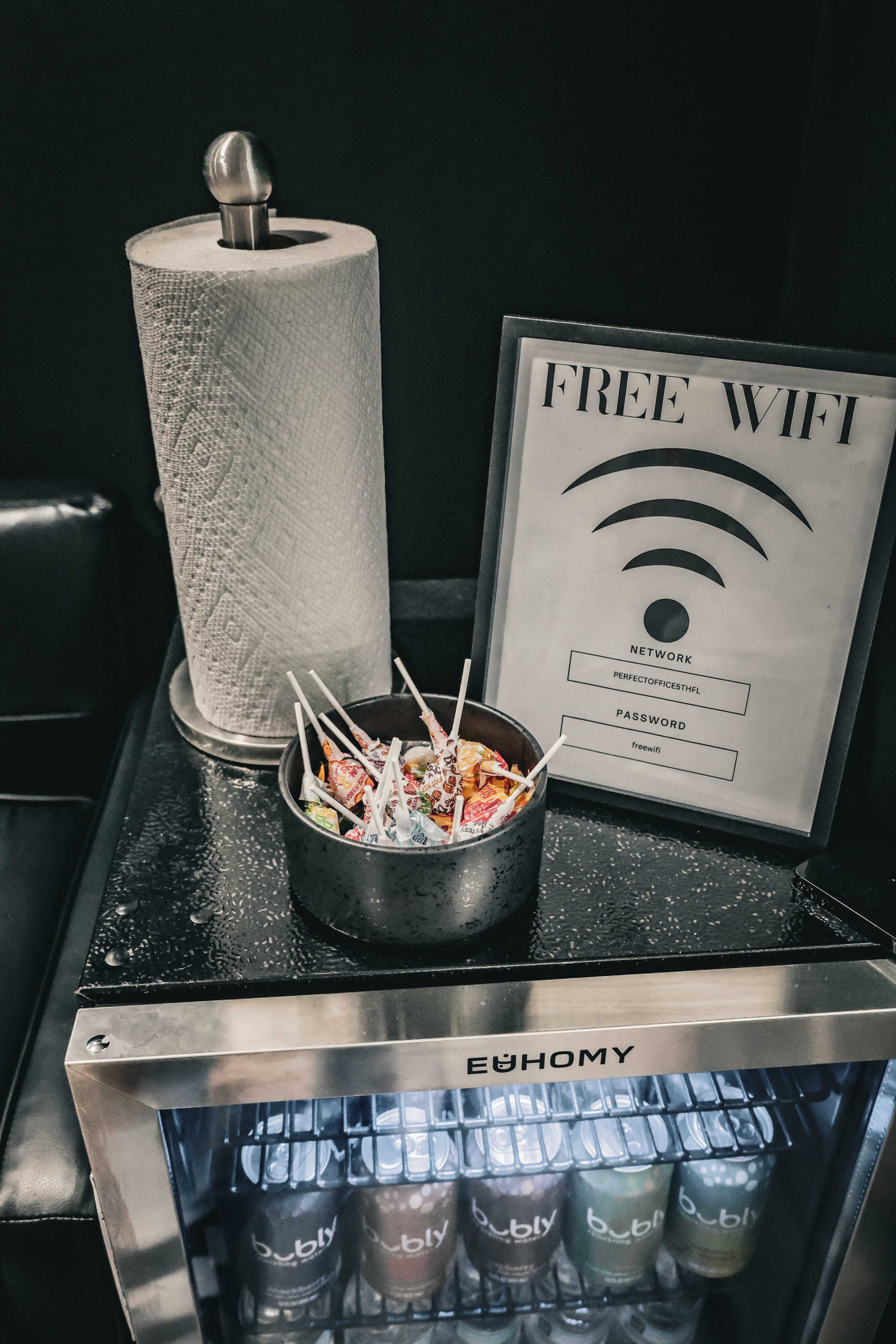 A bowl of colorful snacks sits on a black counter next to a sign displaying the free Wi-Fi network and password.