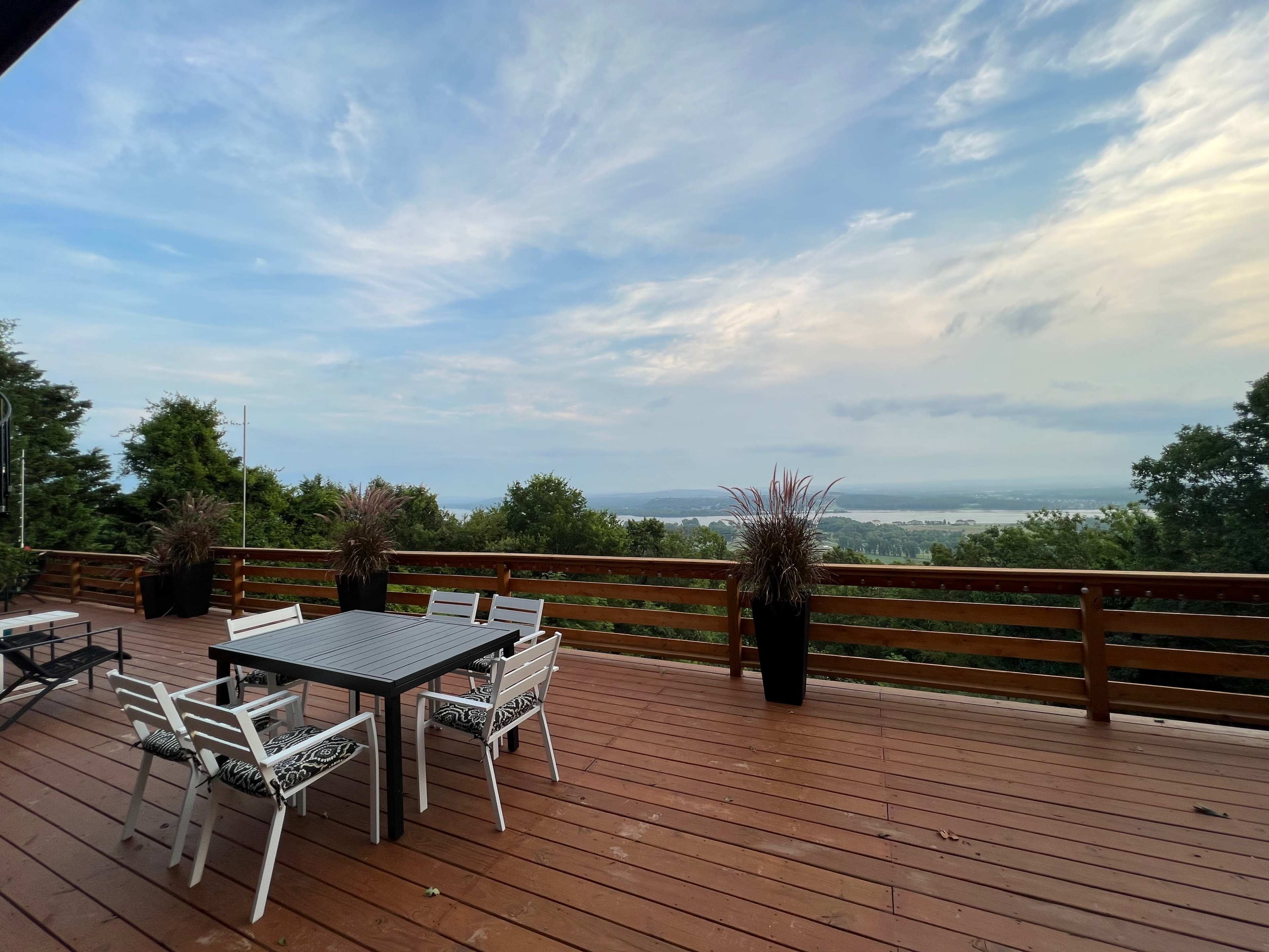 A wooden deck with a table and chairs overlooks a vast landscape under a cloudy sky.