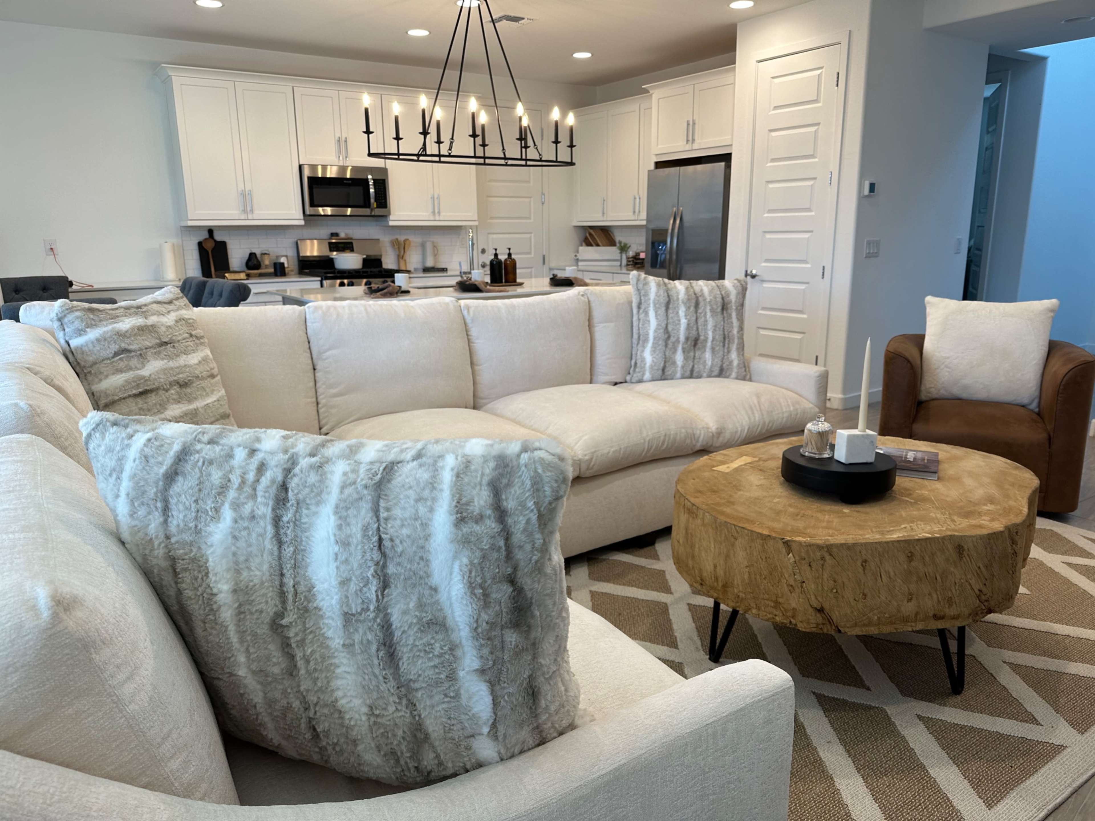 A modern living room with a large sectional sofa, a wooden coffee table, and a well-equipped kitchen visible in the background.