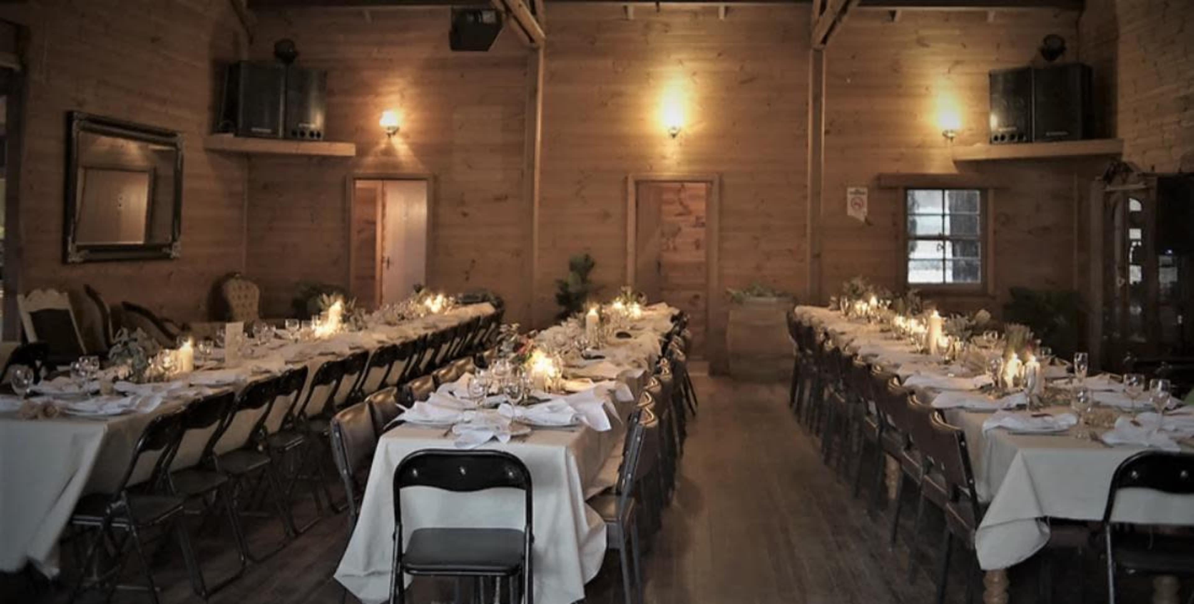 A long hall features neatly arranged tables set for a formal dinner, with candlelight illuminating the wooden interior.