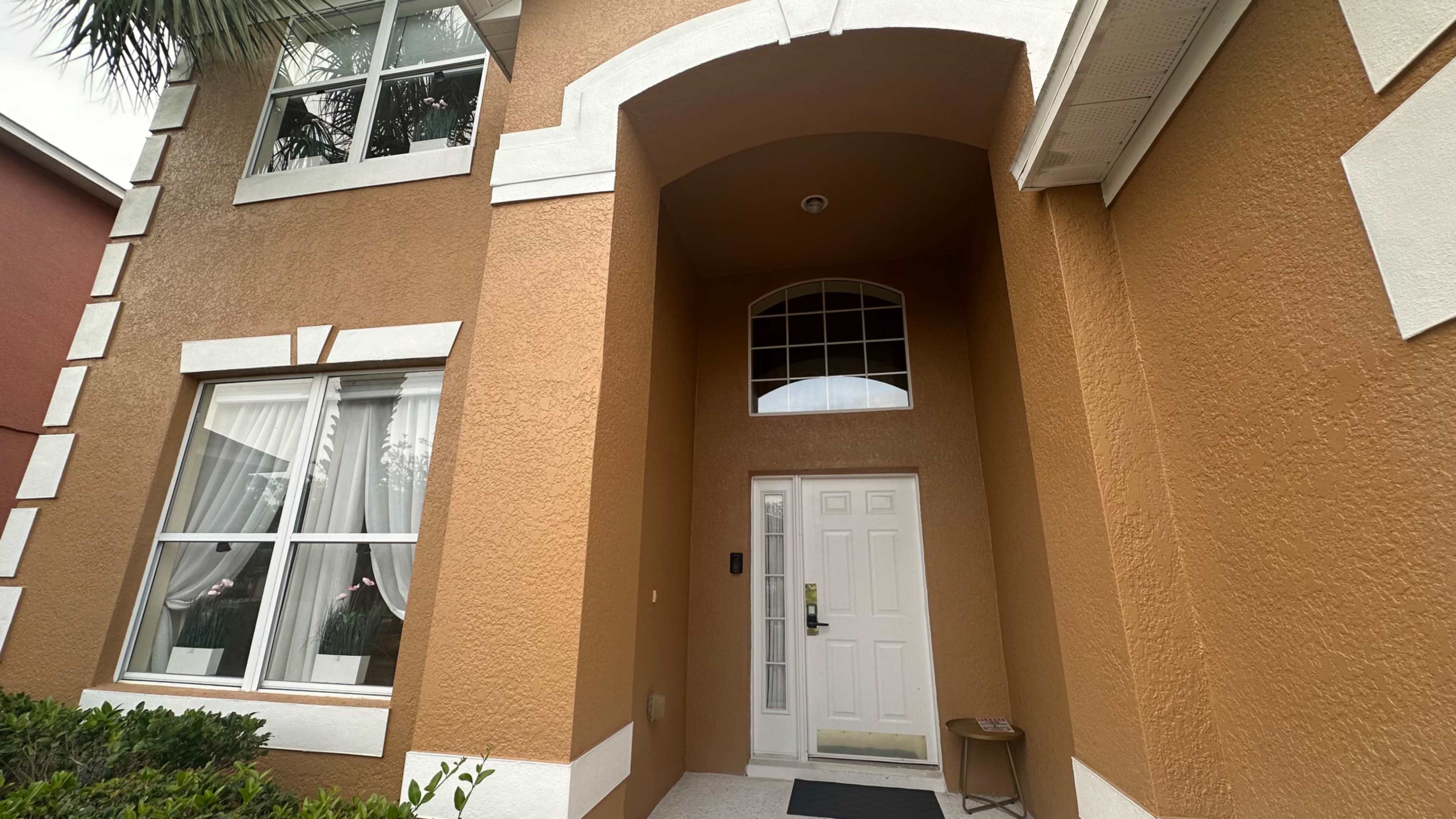 The image shows the entrance of a two-story house with a prominent archway and a white front door surrounded by large windows.