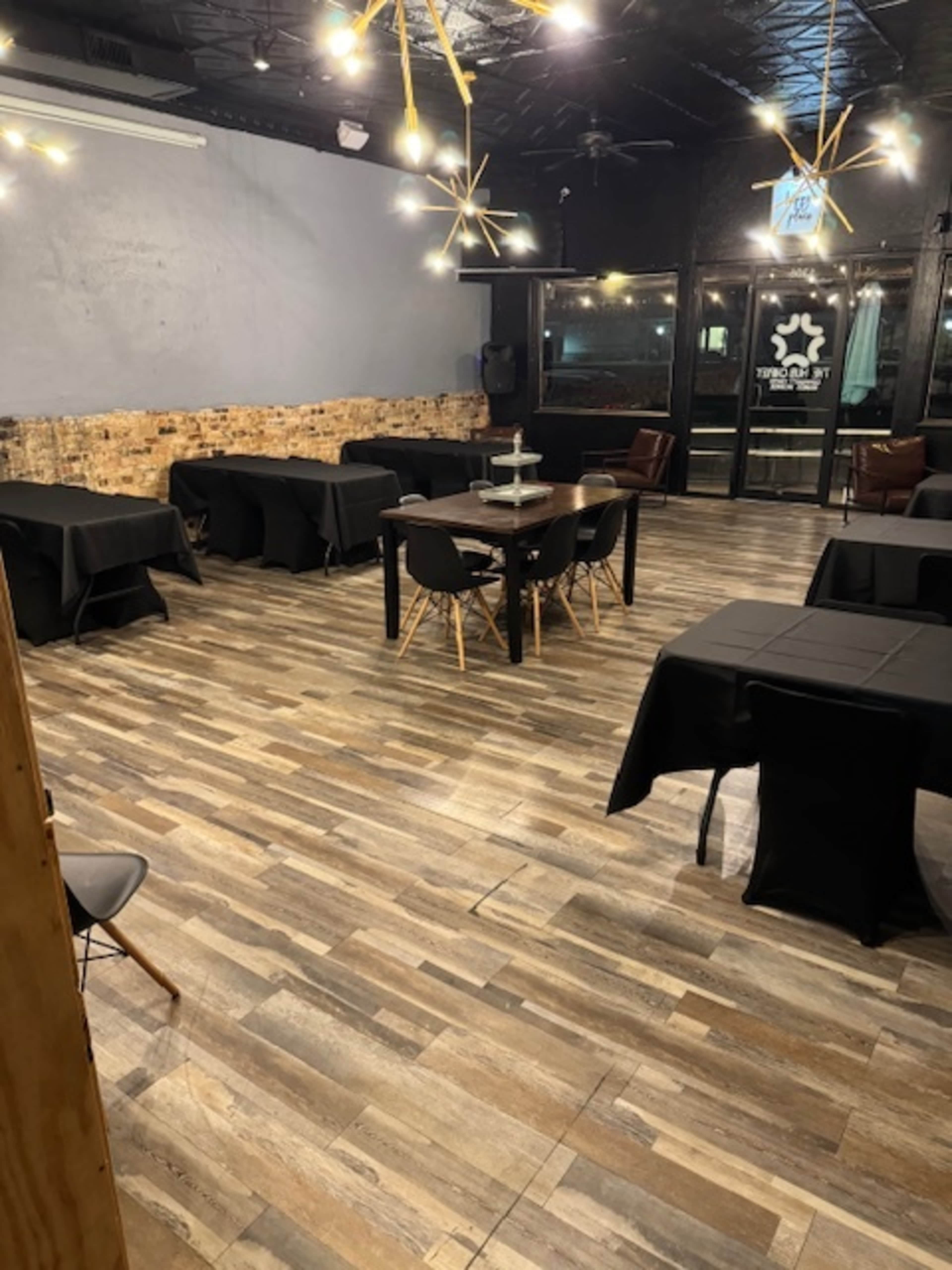 The image shows a spacious restaurant interior with several black tables set up and a decorative lighting feature on the ceiling.