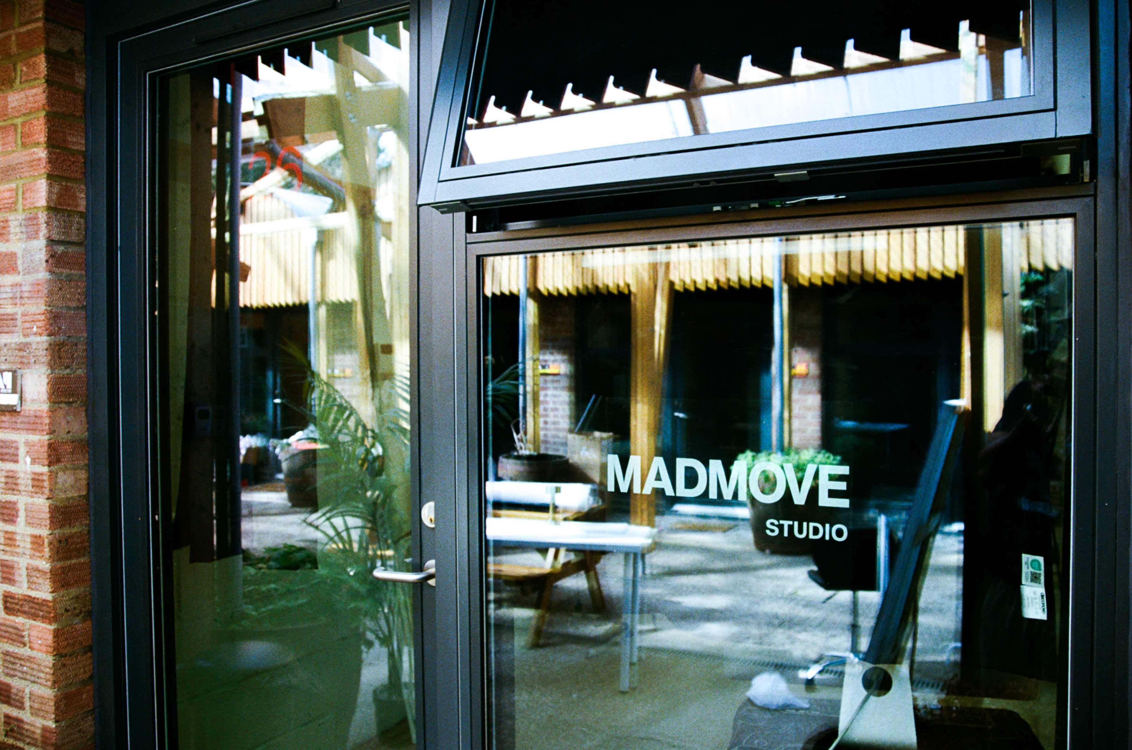 A glass door with the text "MADMOVE STUDIO" reflects the outdoor courtyard and furniture inside.
