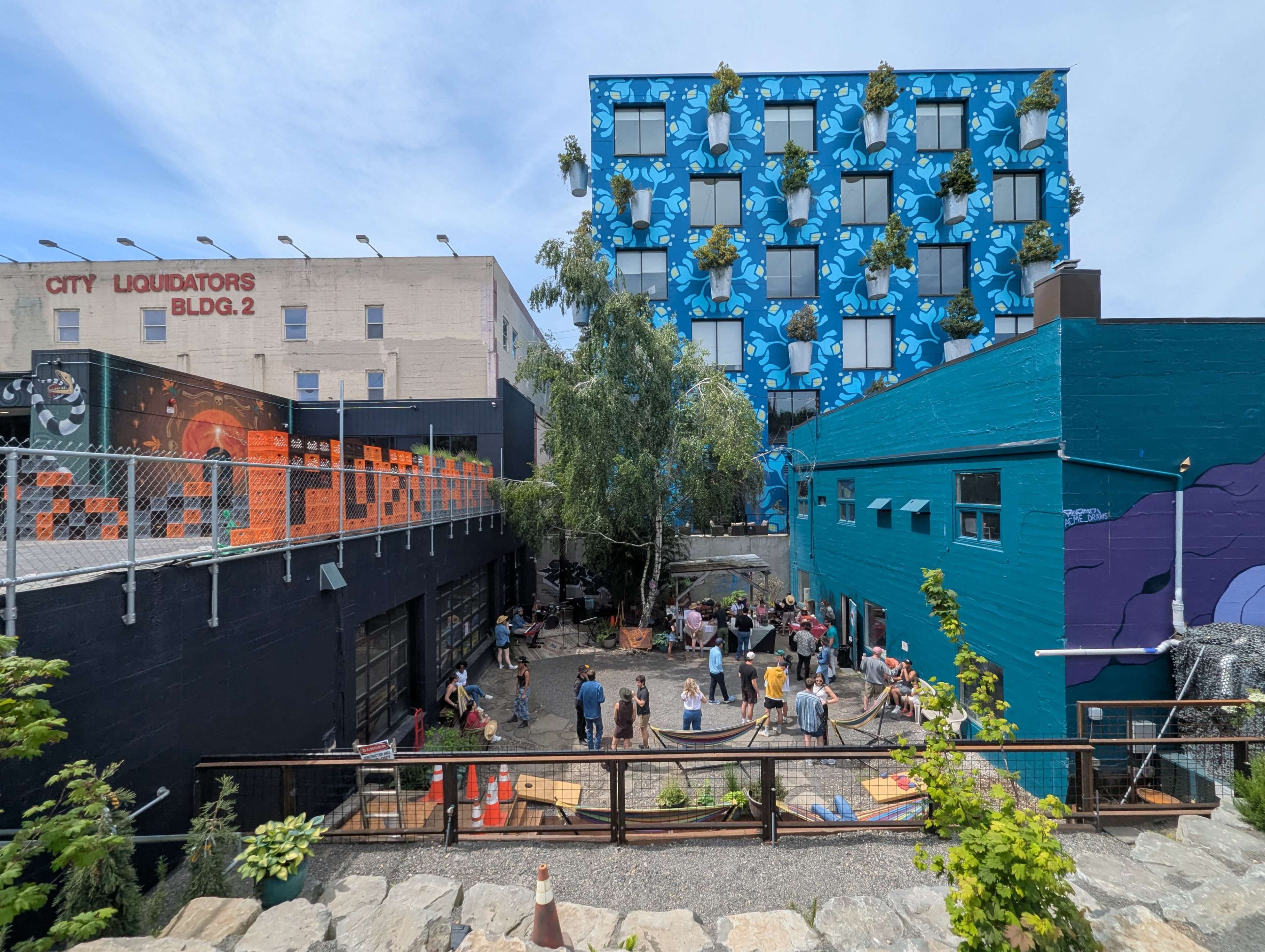 A vibrant urban space features a gathering of people in a courtyard surrounded by colorful buildings and greenery.
