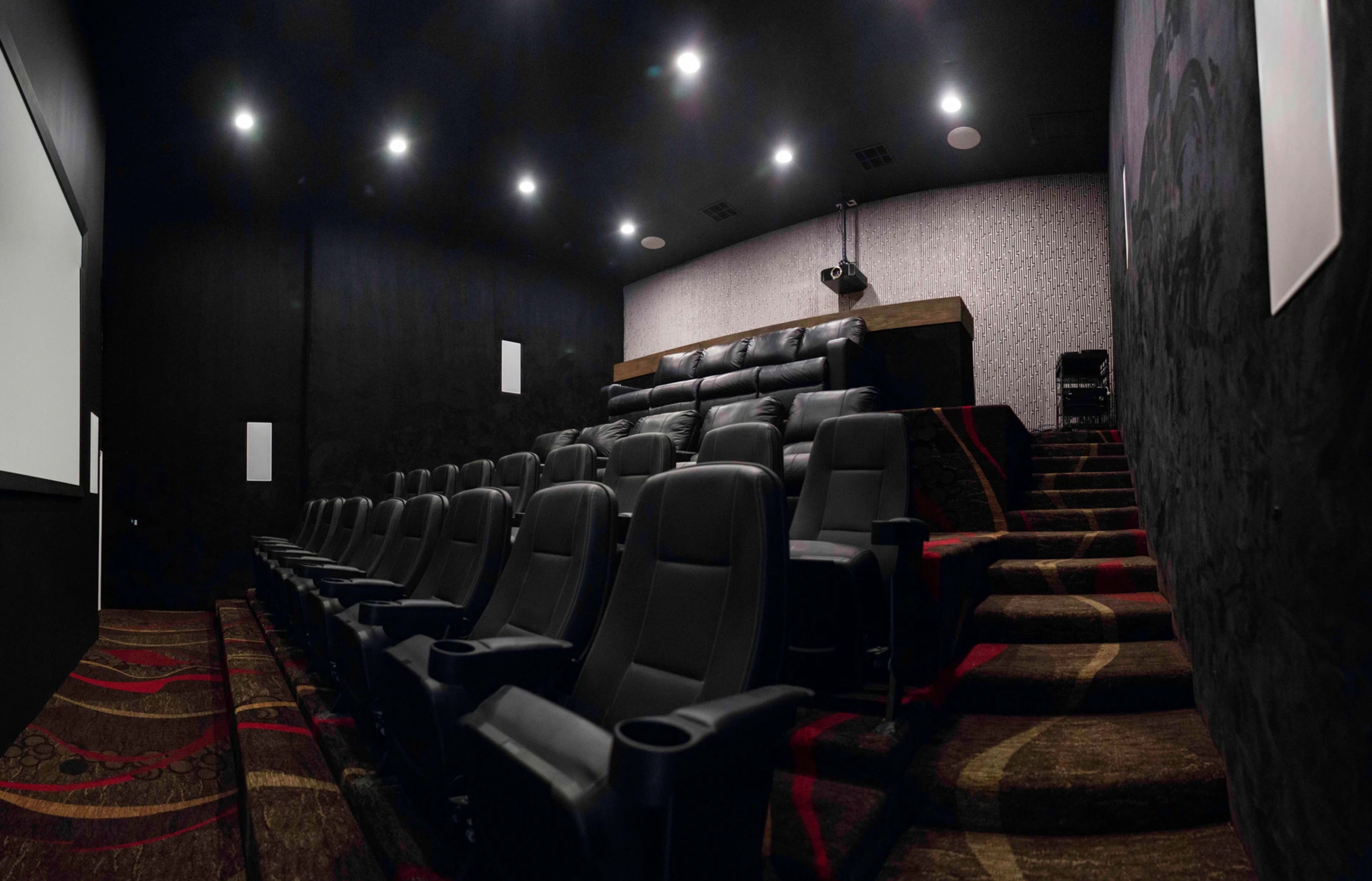 A small, dimly lit movie theater with tiered seating featuring black leather chairs.
