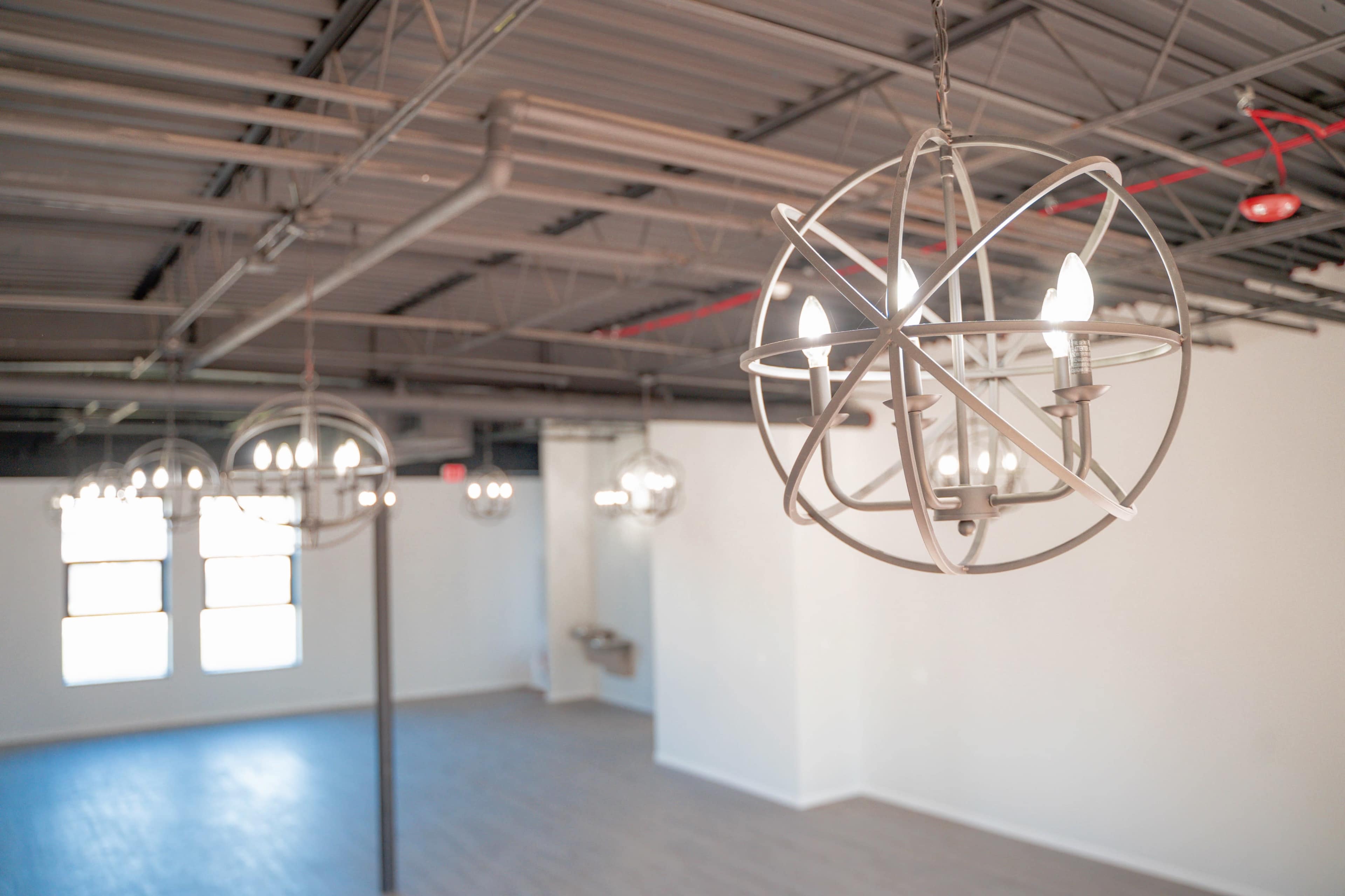 A spacious room with modern pendant chandeliers hanging from the ceiling and large windows allowing natural light to enter.