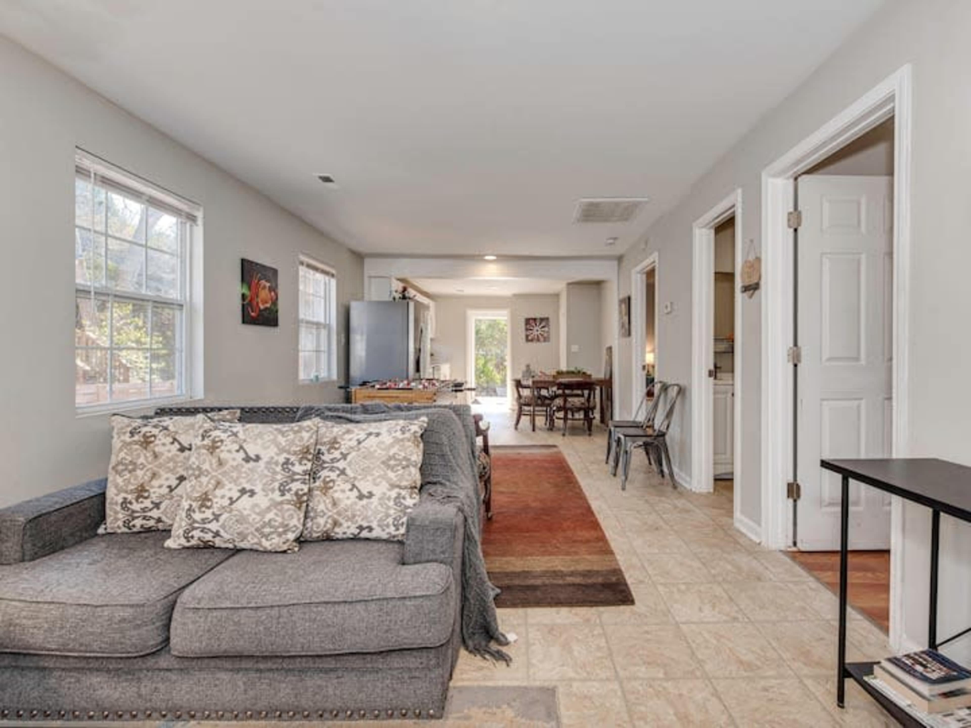 A well-lit living space with a gray couch, an open layout leading to a dining area, and multiple doorways leading to different rooms.