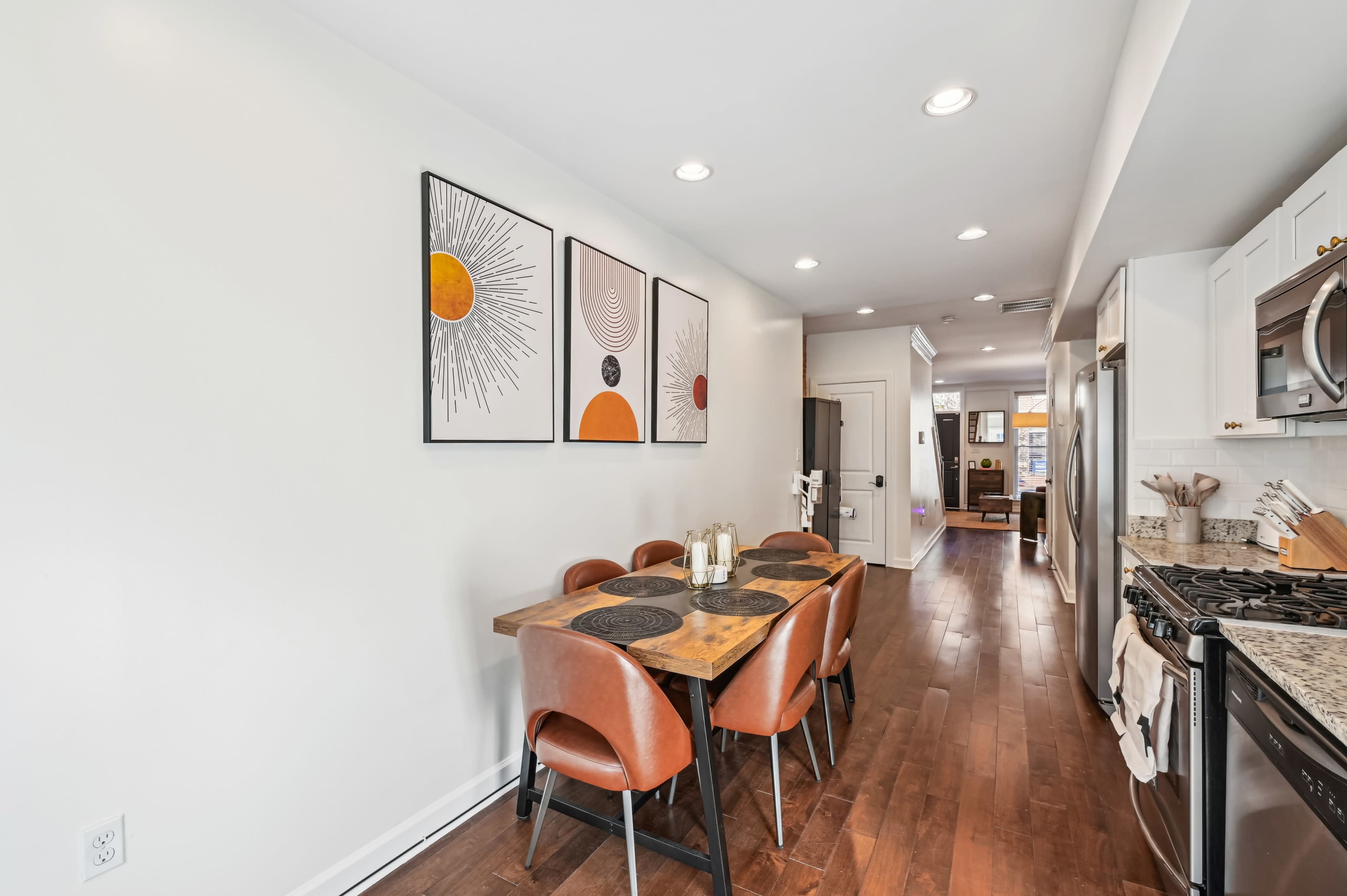 A modern dining area with a wooden table surrounded by brown chairs, and three framed abstract artworks on the wall.