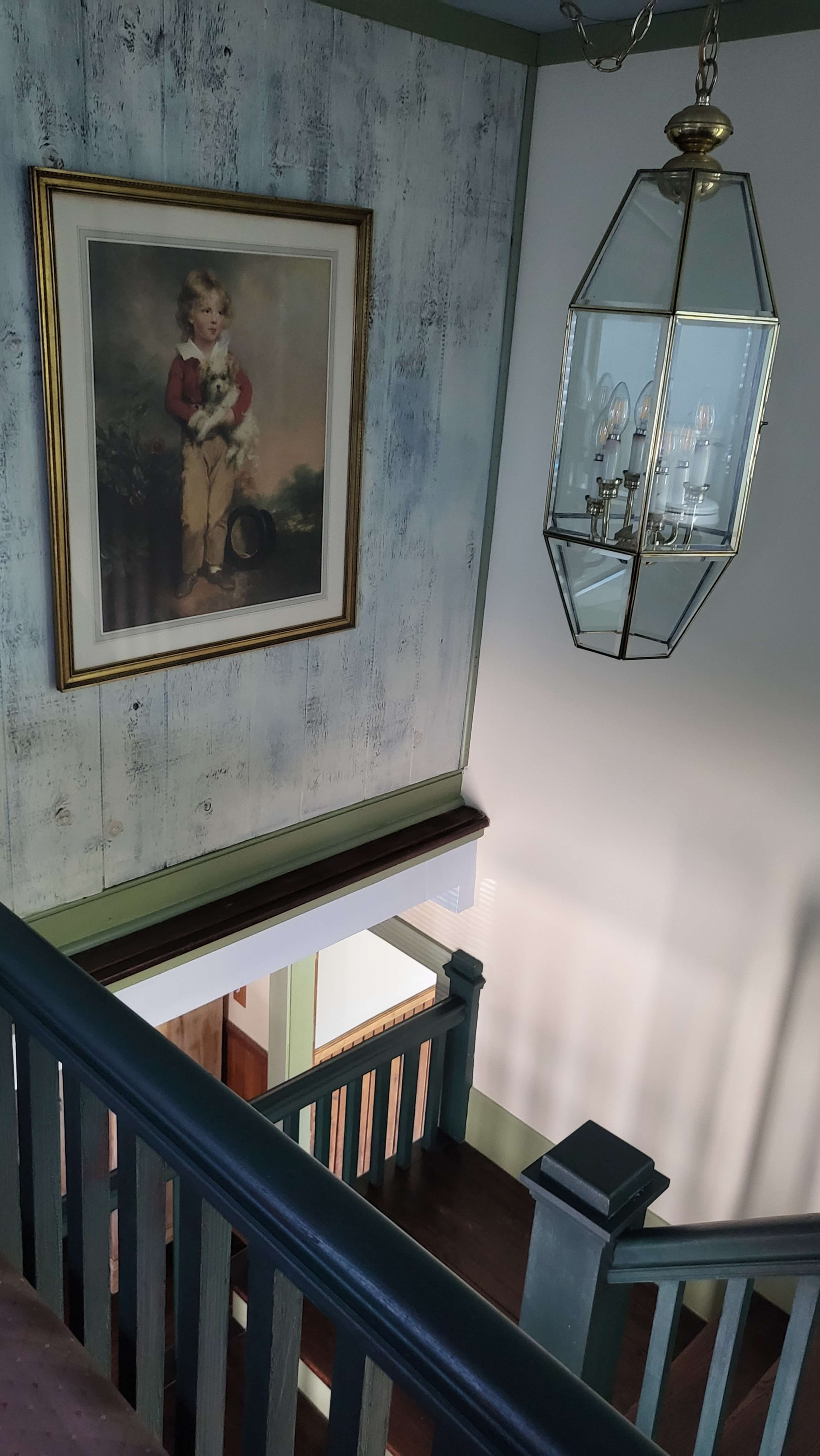 A staircase leading down to a landing with a framed portrait of a boy holding a cat and a glass pendant light overhead.